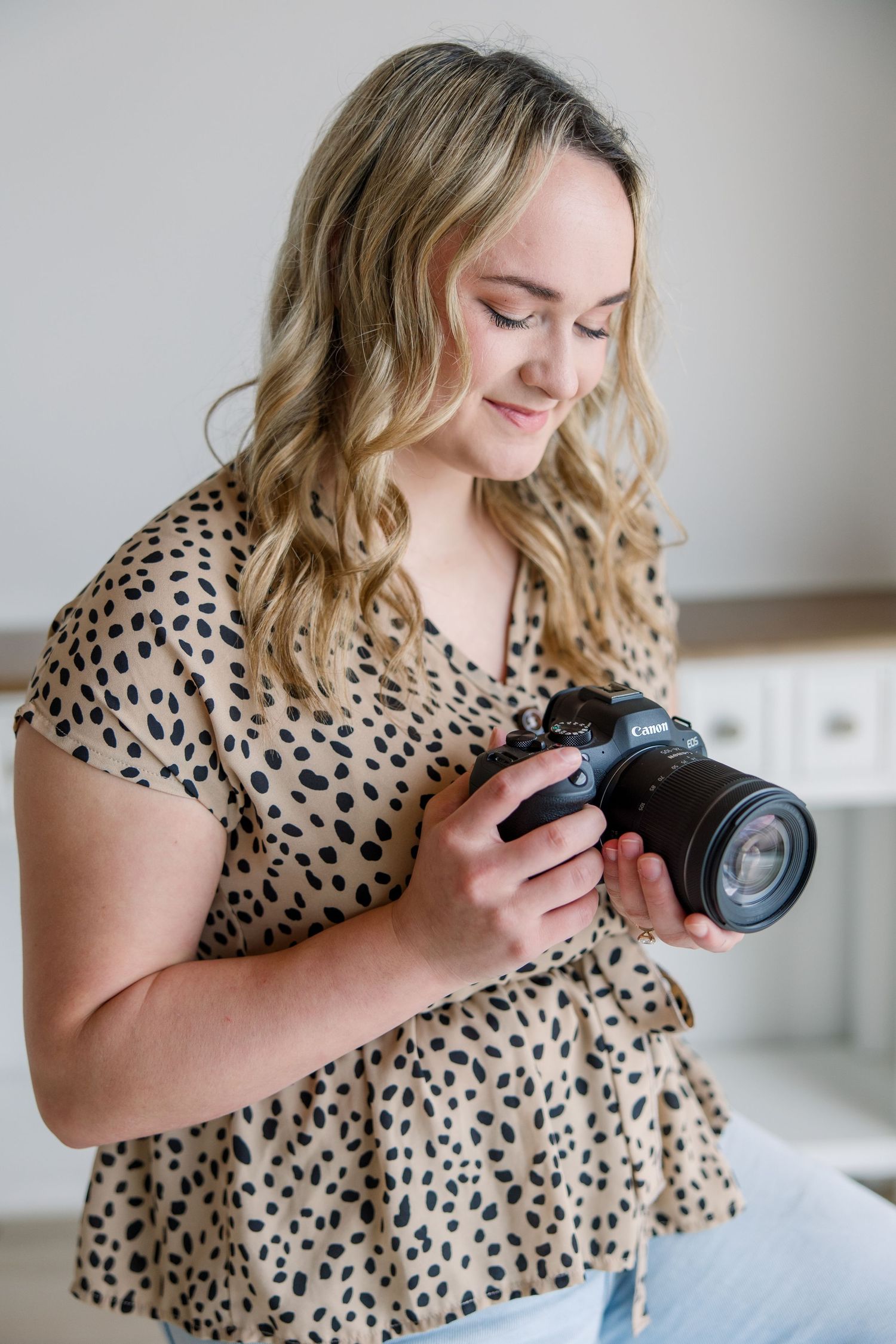 Photographer in polka dot dress examines camera settings while working in bright interior space.