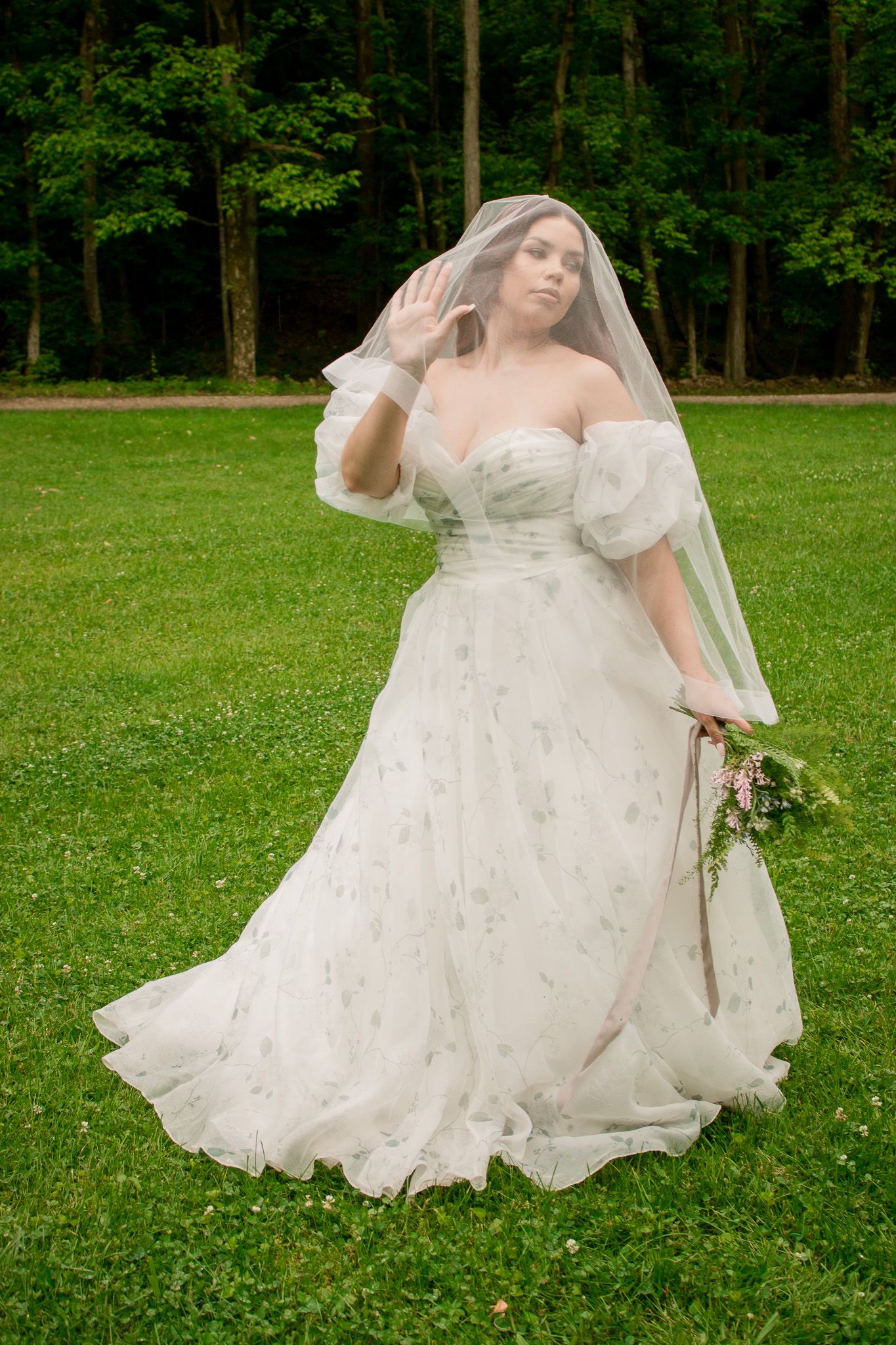 A bride in a flowing white gown twirls gracefully on a lush green lawn with trees in the background.
