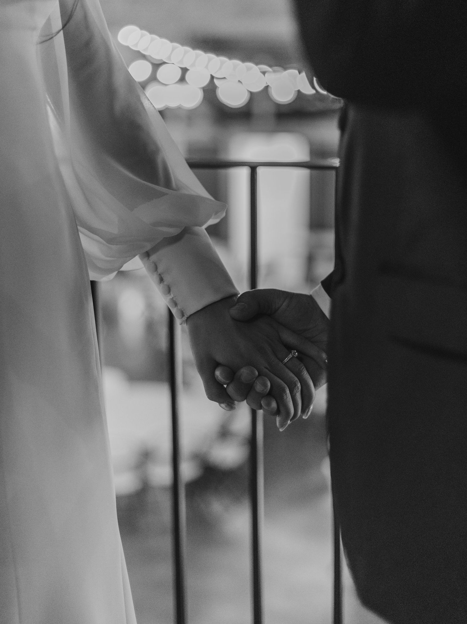 A black and white close-up photograph of two hands clasped together in an intimate gesture.