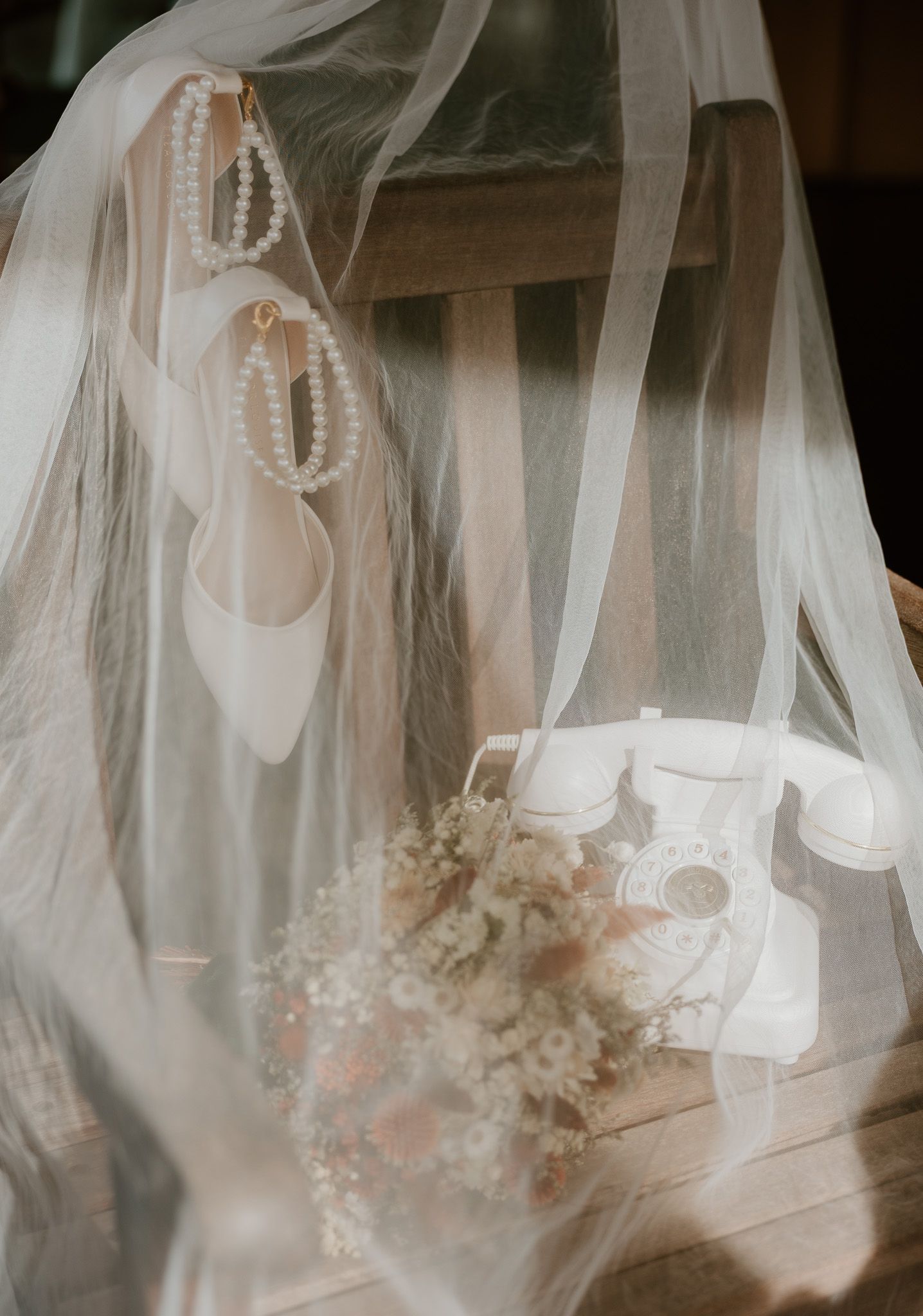A row of delicate white wedding veils with pearl details hanging on display in soft lighting.
