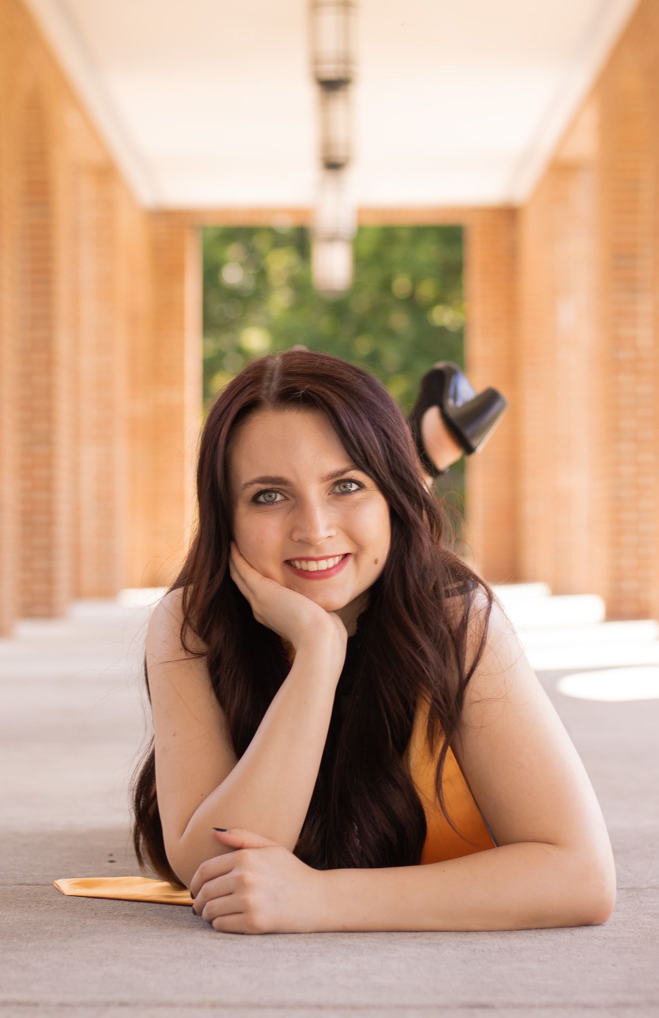 A person with dark hair lying on the ground in a warm-toned setting with columns visible in the background.