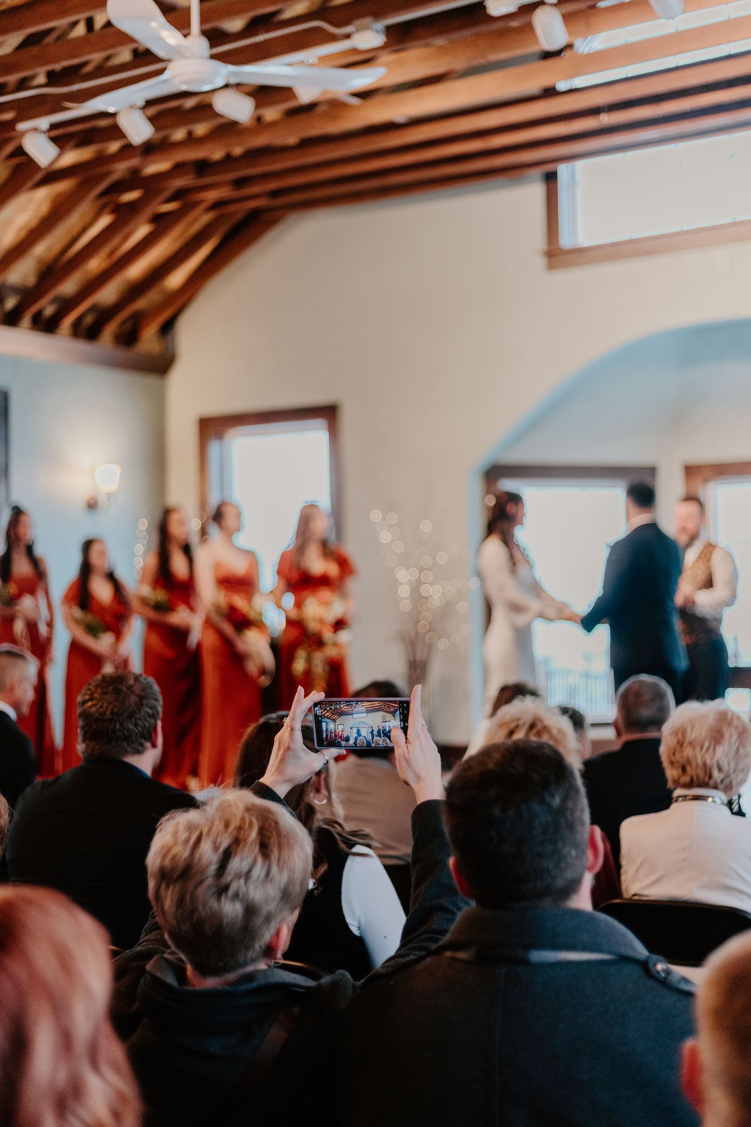 A panoramic view of a crowded indoor event venue with exposed wooden beams on the ceiling and people seated in rows.