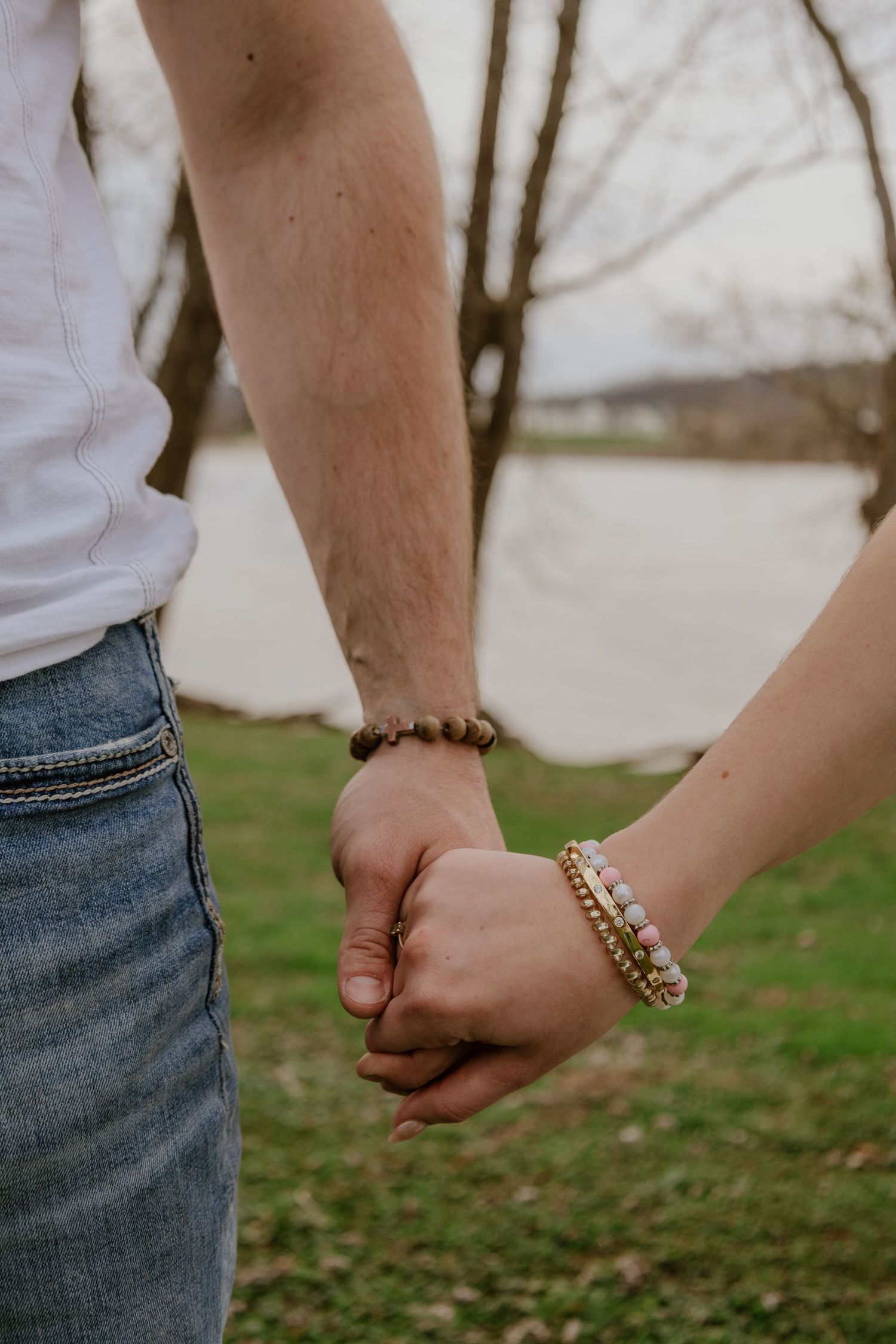 Close-up of two people holding hands with beaded bracelets against a blurred outdoor background.
