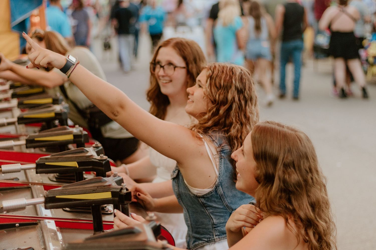 People pour wine samples during a tasting event at an indoor venue with warm lighting and blurred background.