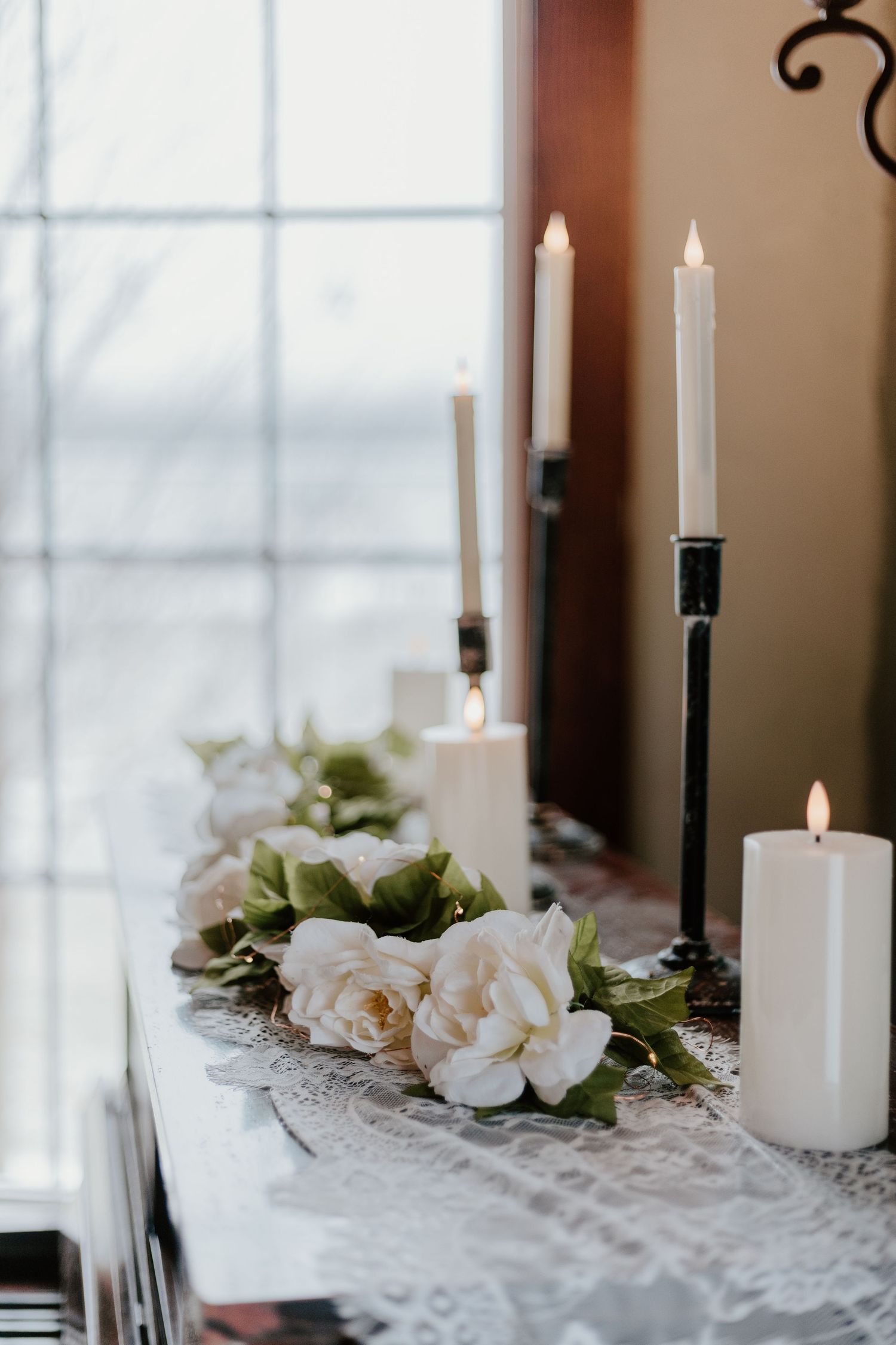 White candles and delicate lace decor create an elegant tablescape with soft floral accents and natural light.