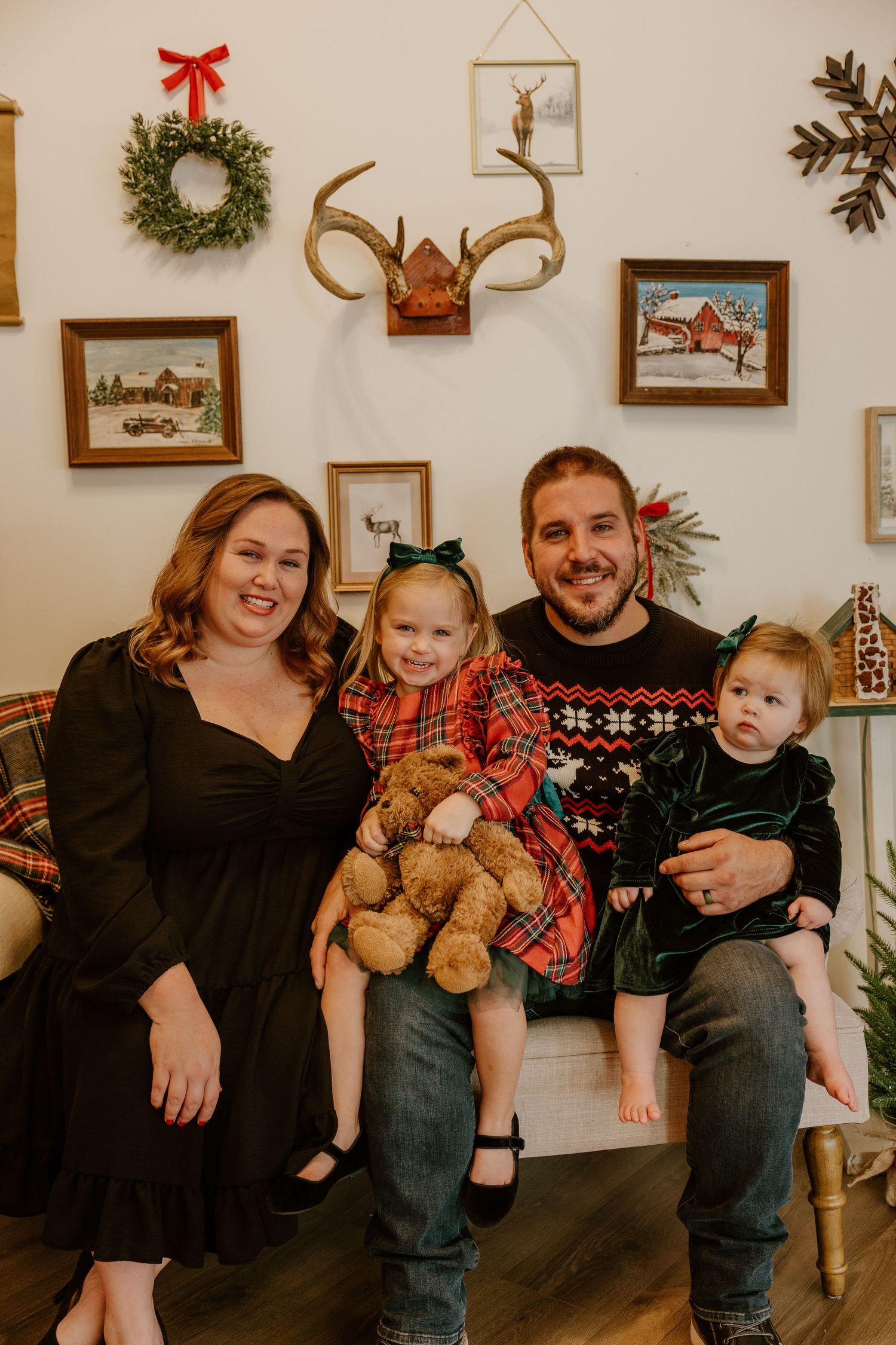 A family poses together in front of a wall decorated with holiday wreaths and framed winter artwork.