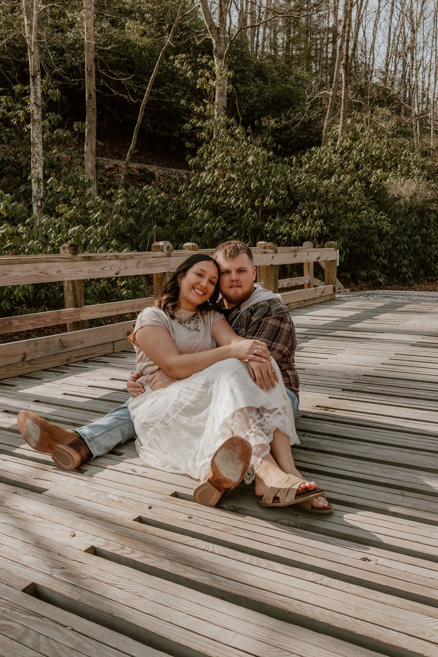 A couple shares an intimate moment while lying on a rustic wooden deck surrounded by trees.