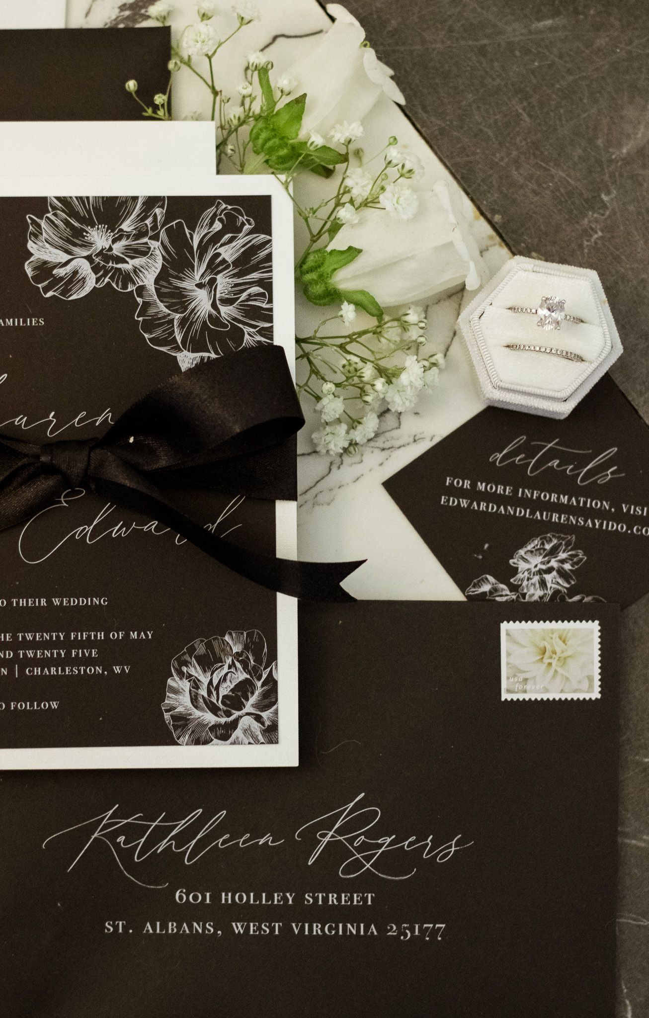 Elegant black and white wedding invitation suite with floral designs and calligraphy on dark background.