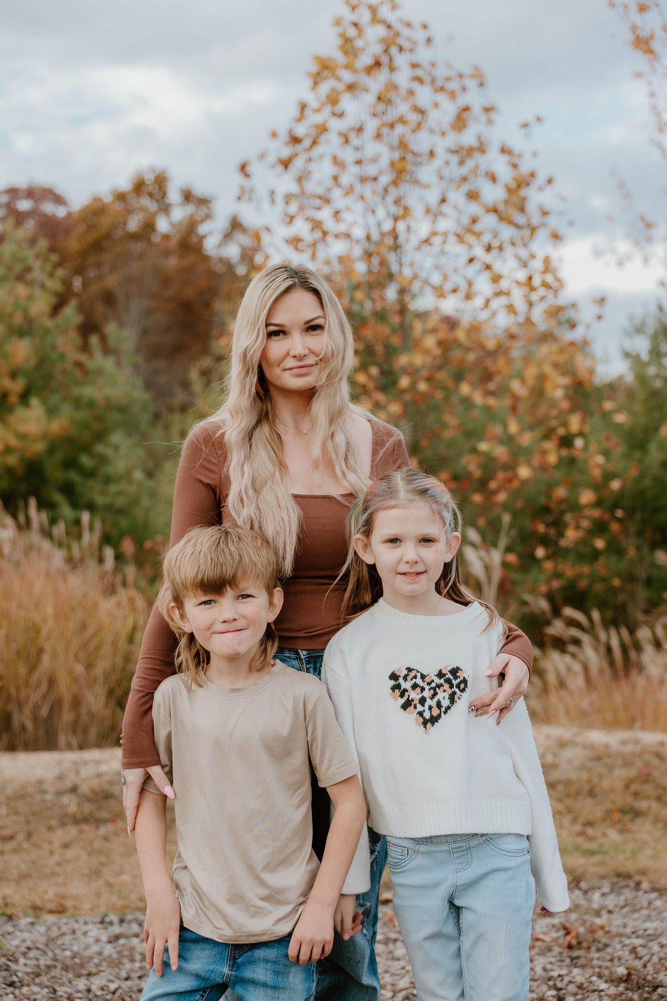 A family poses together outdoors during autumn with fall foliage and warm brown tones in the background.