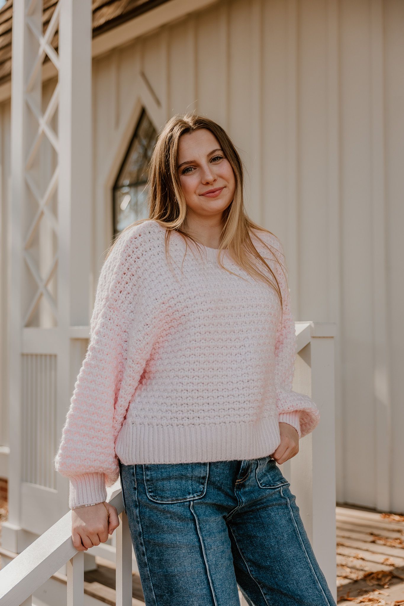 A cozy pink knit sweater paired with blue jeans creates a casual and comfortable outdoor look.