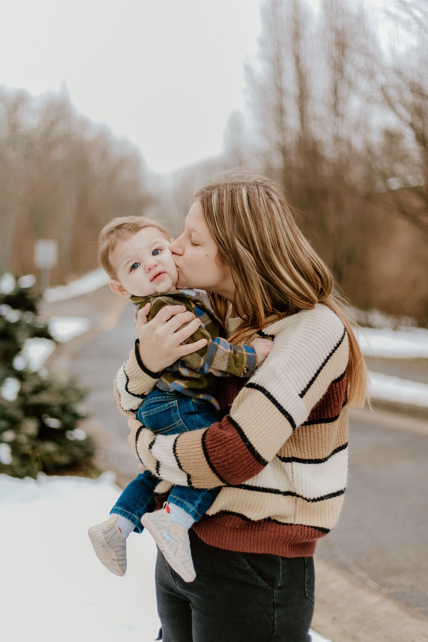 A parent in a striped sweater holds and kisses a baby wearing denim in a series of tender outdoor moments.