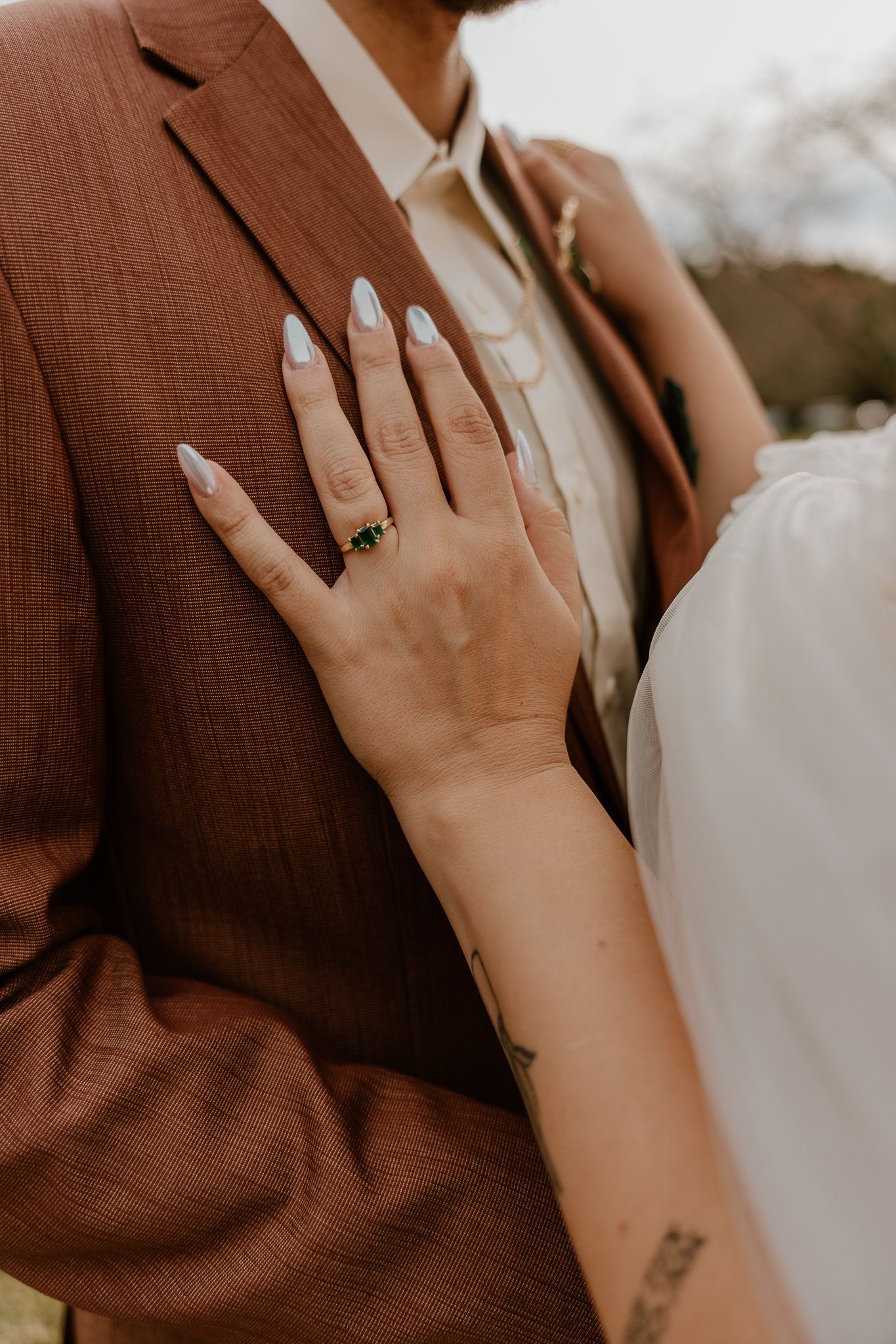 Close-up view of hands wearing engagement rings against a brown and white background.
