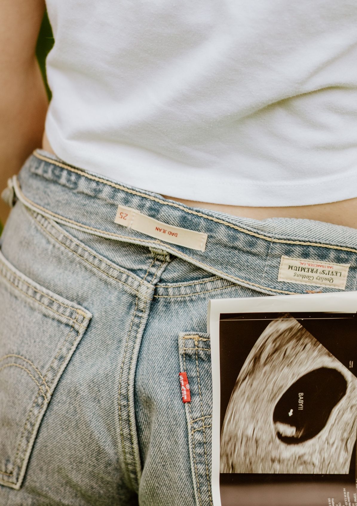 Light wash Levi's jeans with white t-shirt and ultrasound sonogram photo showing pregnancy announcement.