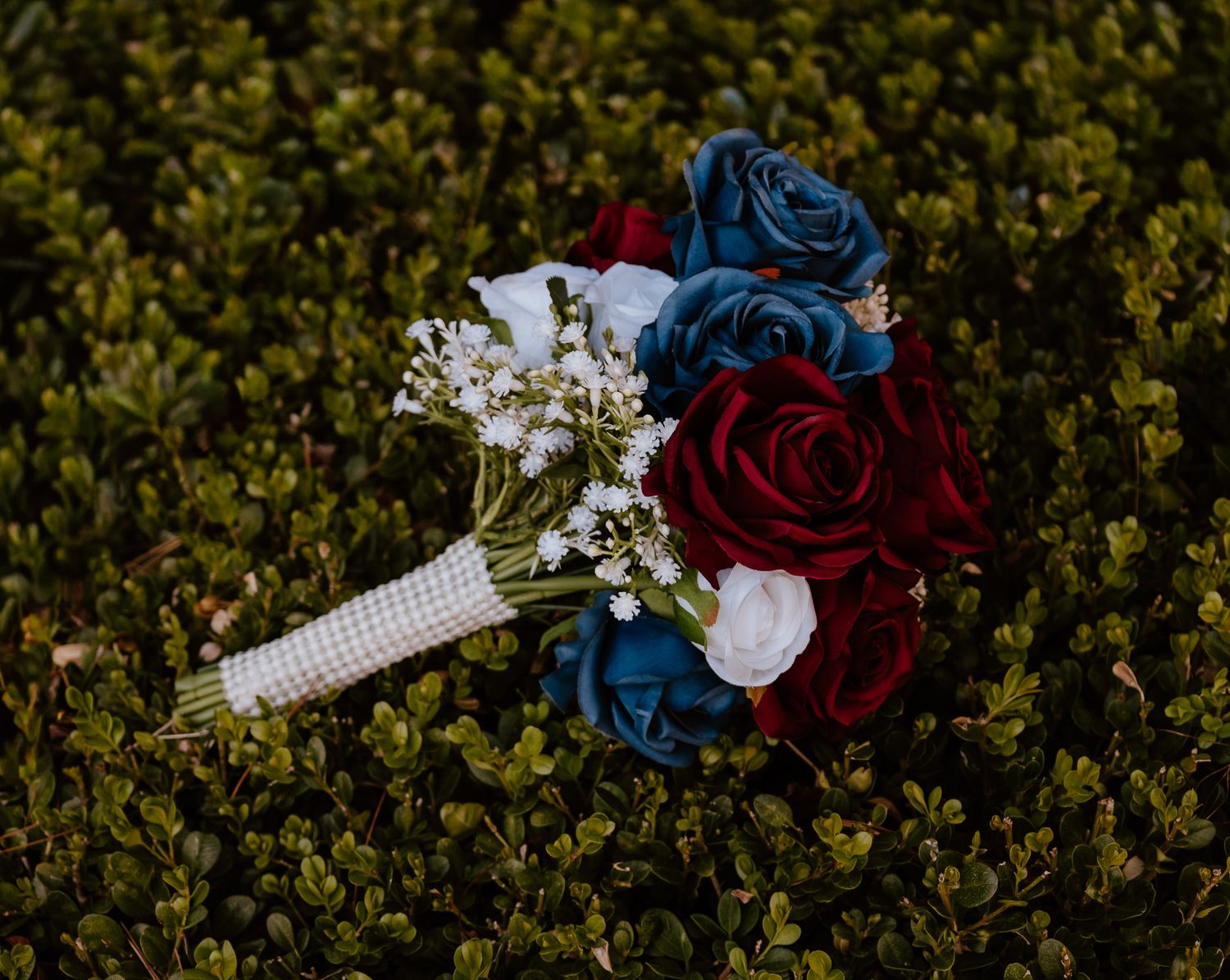 Wedding bouquet with deep red and navy blue roses arranged against a dark green natural background.