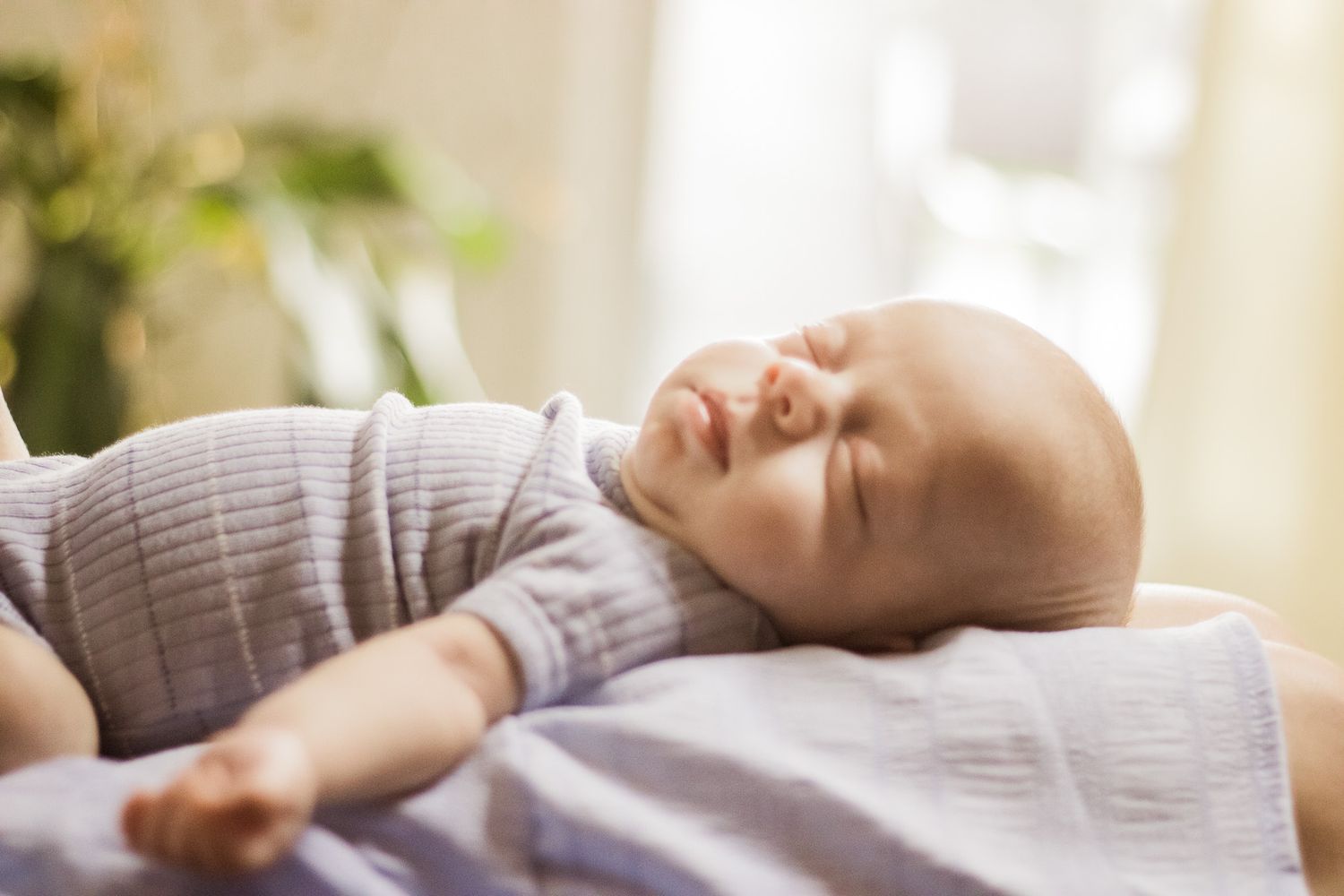 Baby sleeping peacefully on soft white bedding in natural window light.
