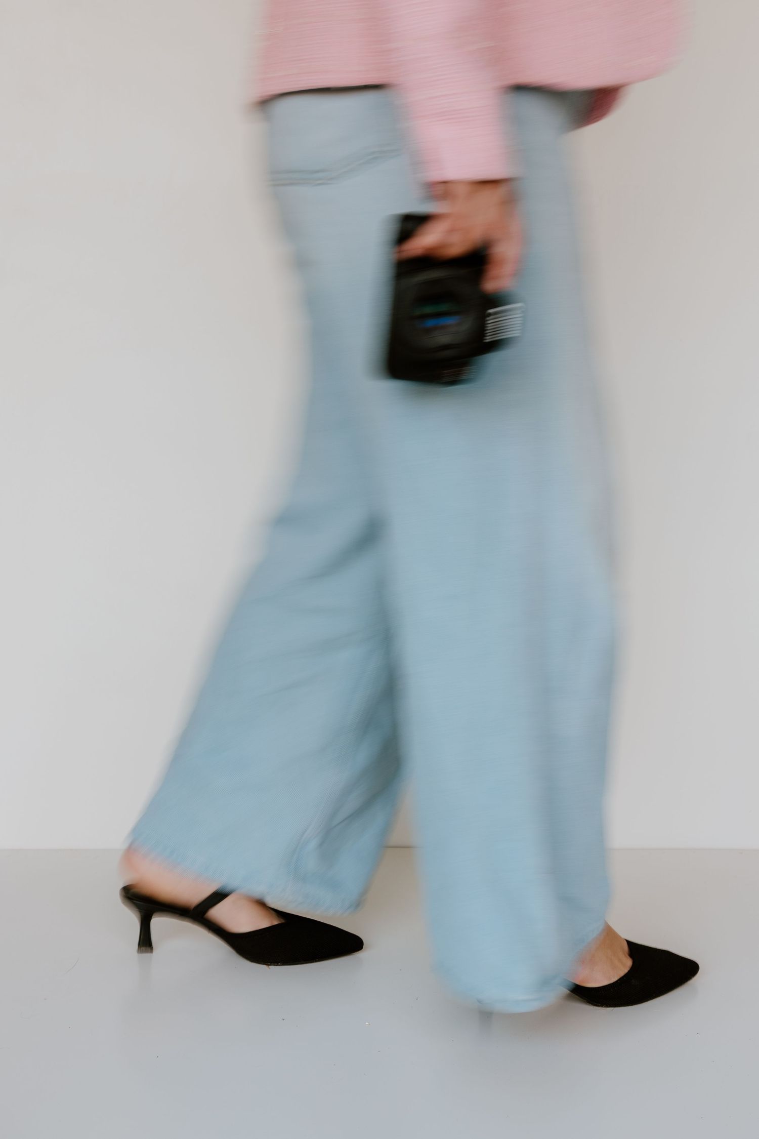 Motion blurred fashion photo showing light blue wide-leg pants paired with black heels and pink top detail.