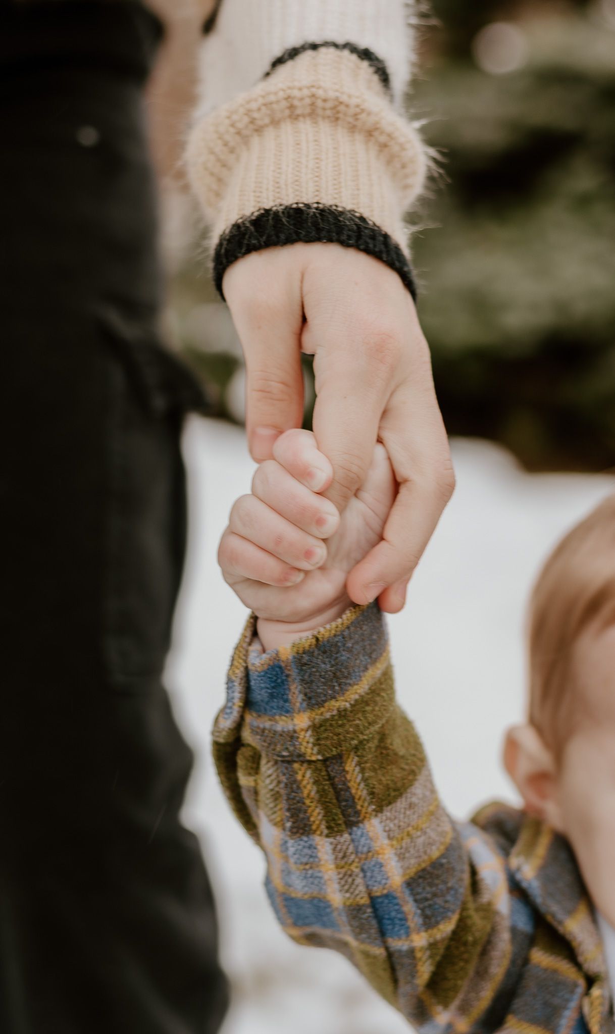 Close-up view of two people holding hands wearing plaid and knit sleeves against a blurred background.