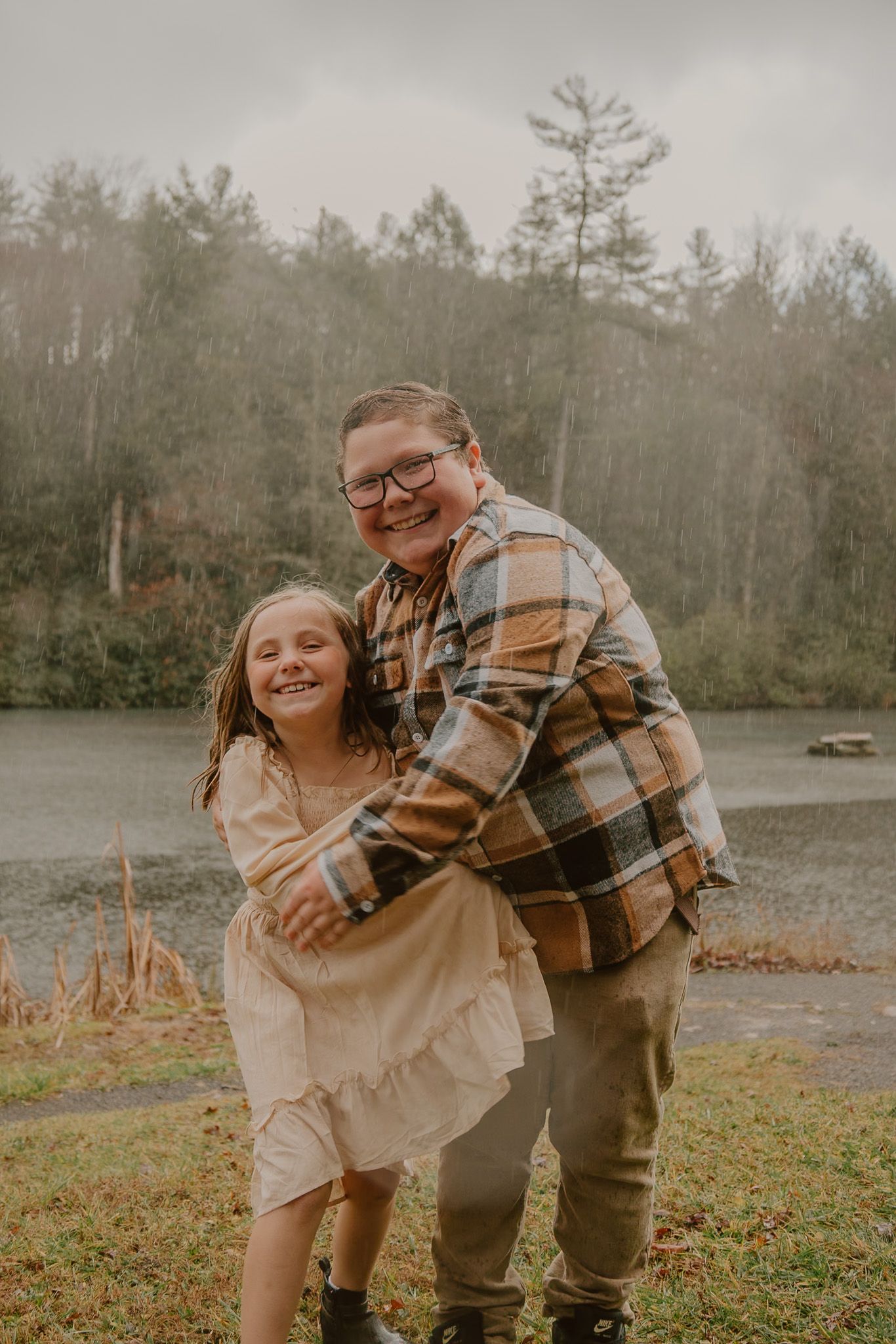 A playful outdoor photoshoot with people in matching plaid and beige outfits laughing together by a lake.