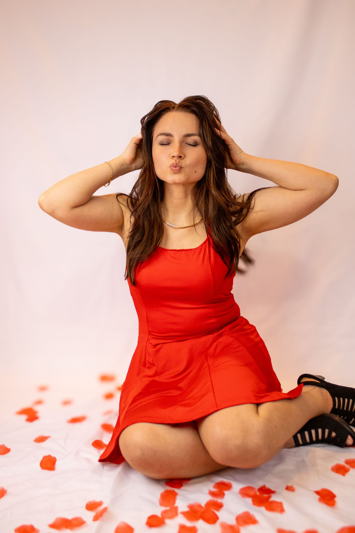 Woman in red dress poses gracefully on floor surrounded by scattered red paper hearts in romantic Valentine's Day setting.