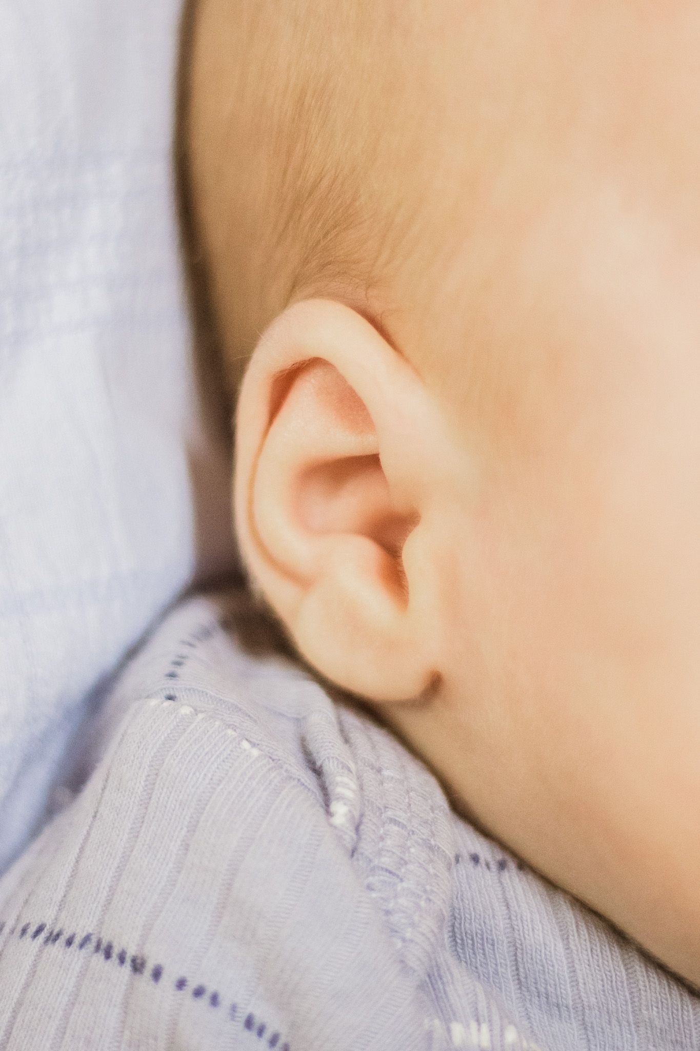 Close-up of a baby's ear wearing a soft gray knit outfit while resting peacefully.