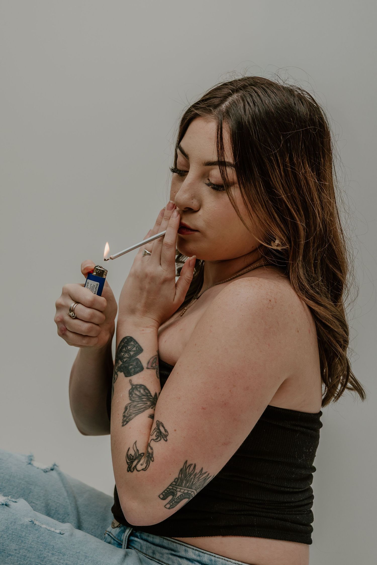A series of artistic photos showing a person with butterfly tattoos smoking against a gray background.