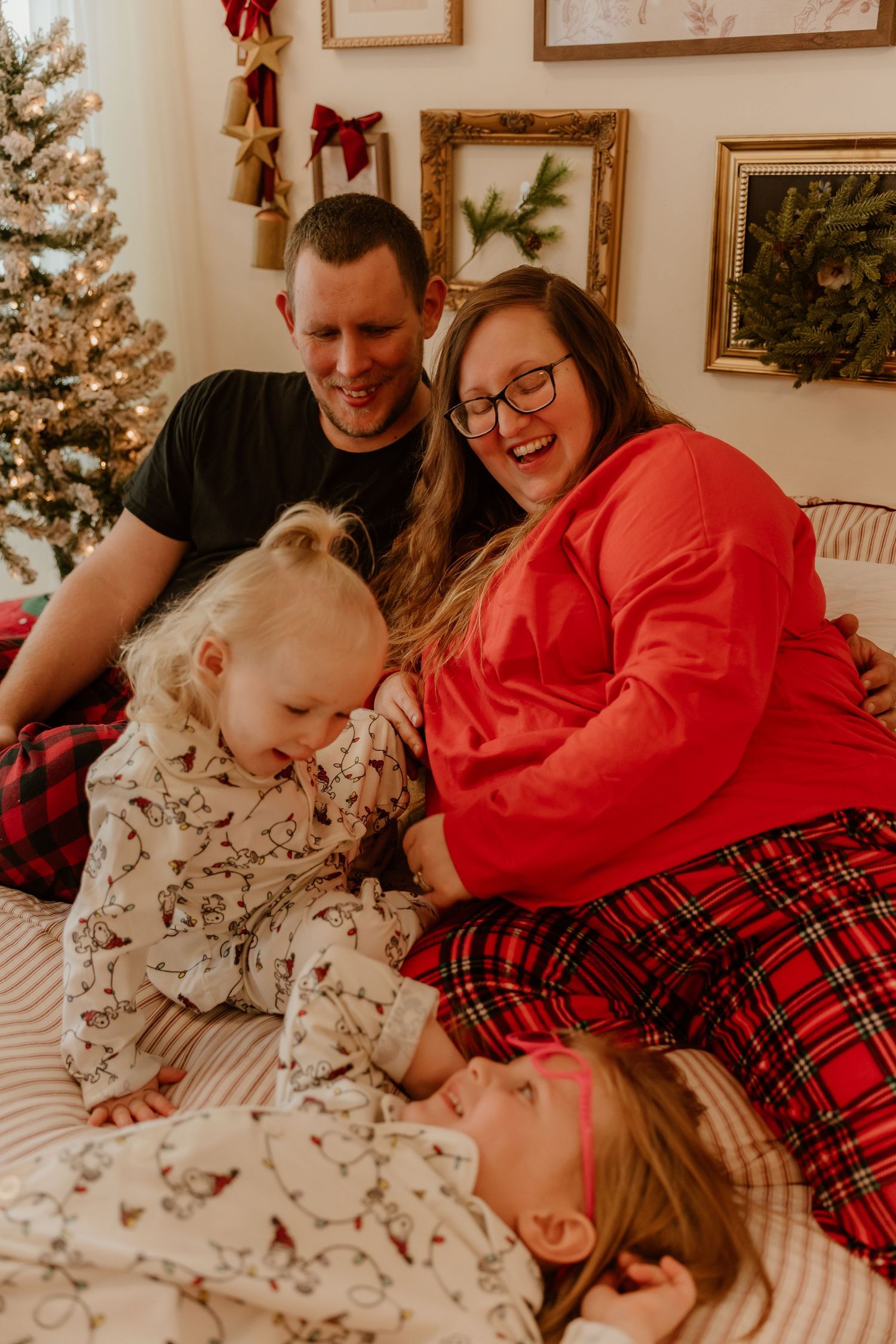 A family shares joyful laughter while relaxing together in matching holiday pajamas near a decorated Christmas tree.