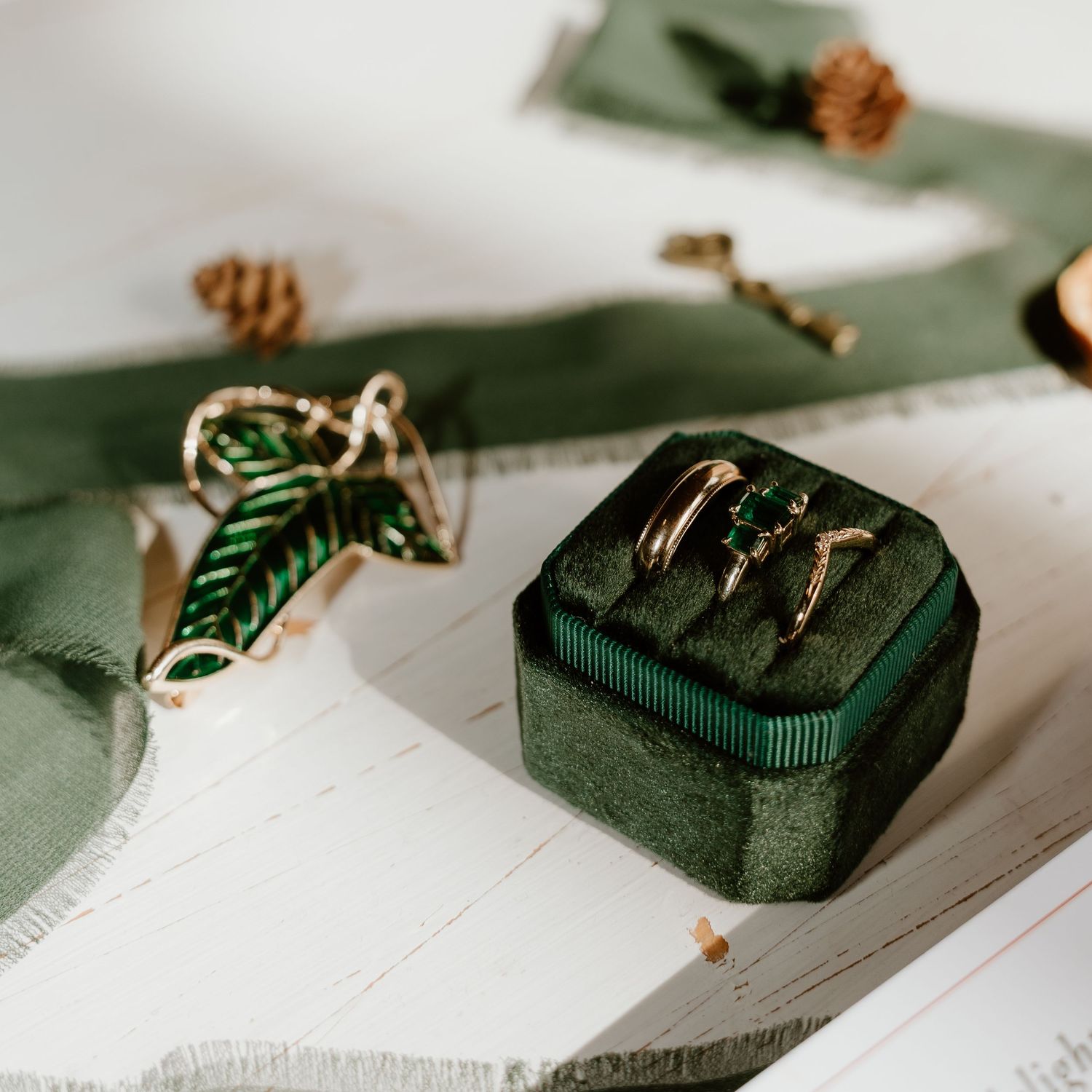 Green velvet ring box with gold wedding bands displayed on white paper in an elegant arrangement.