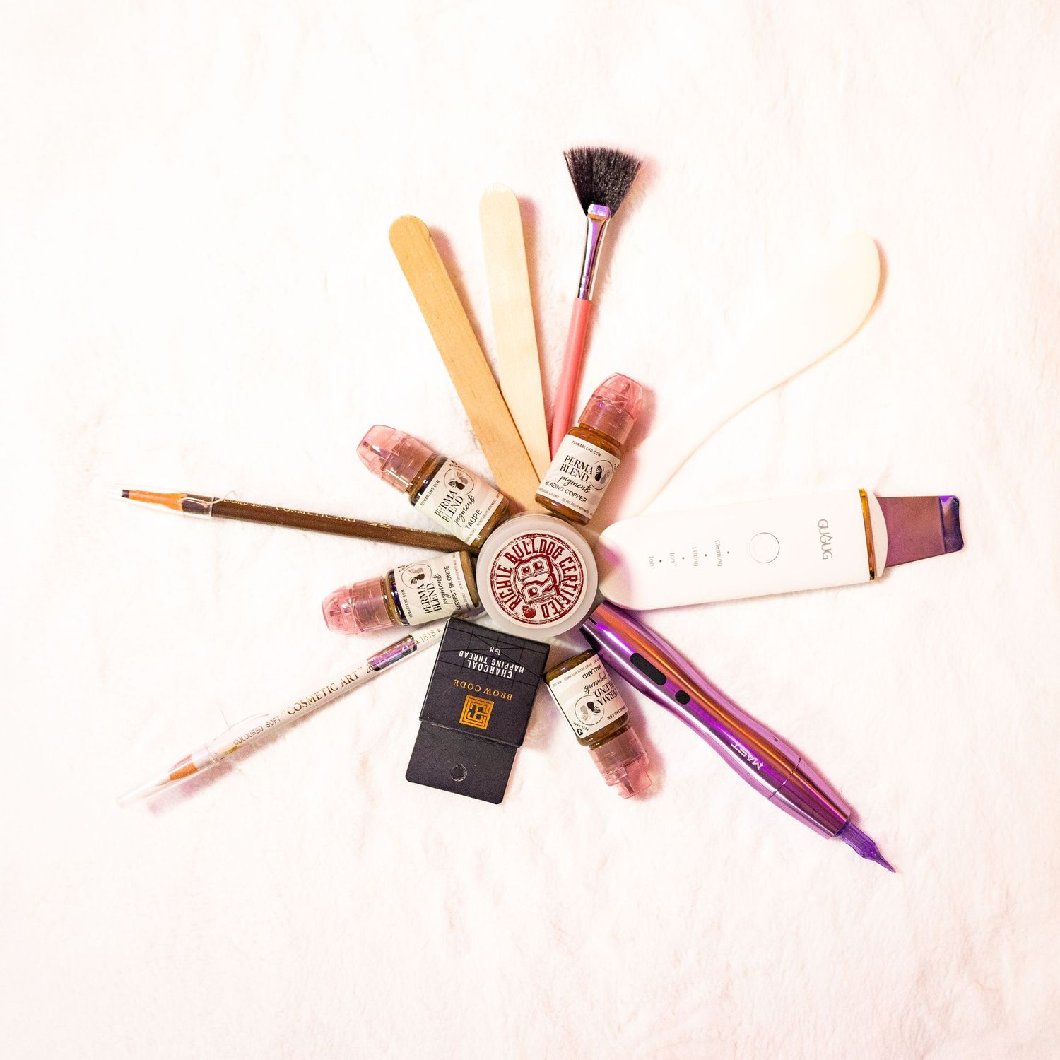 Makeup brushes and beauty products arranged in a fan shape on white background with soft pink lighting.