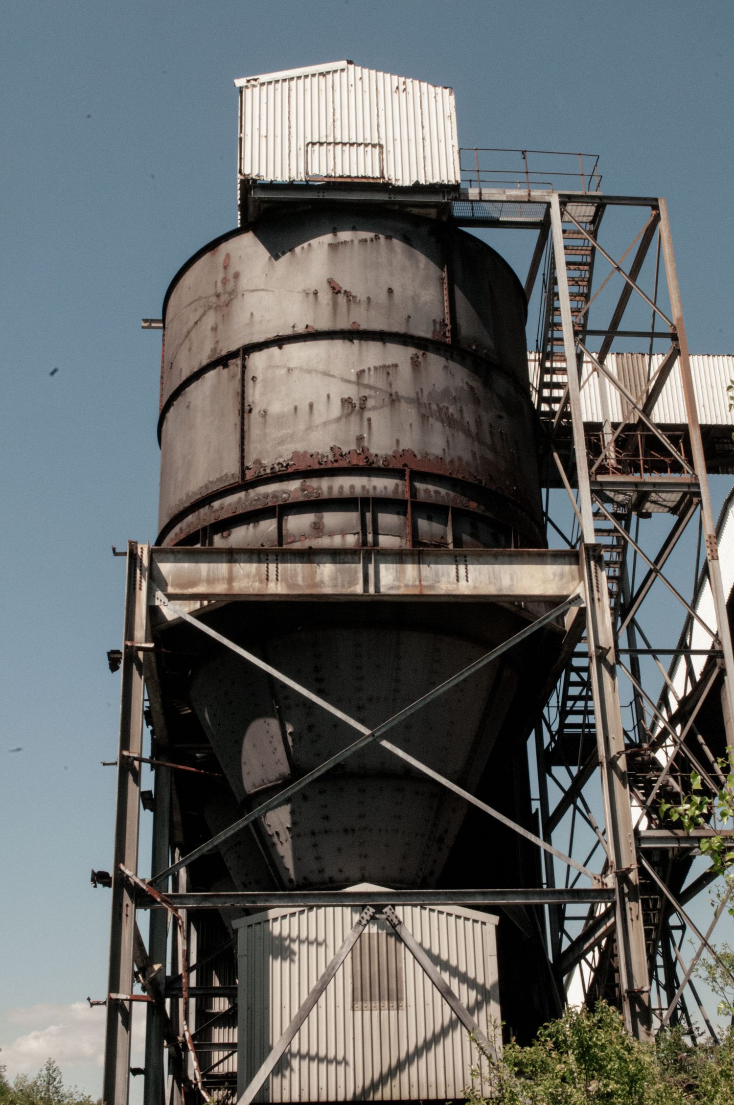 Tall rusted industrial tower with cylindrical tanks and metal framework, standing against a bright blue sky  cwm coke works beddau ash olion