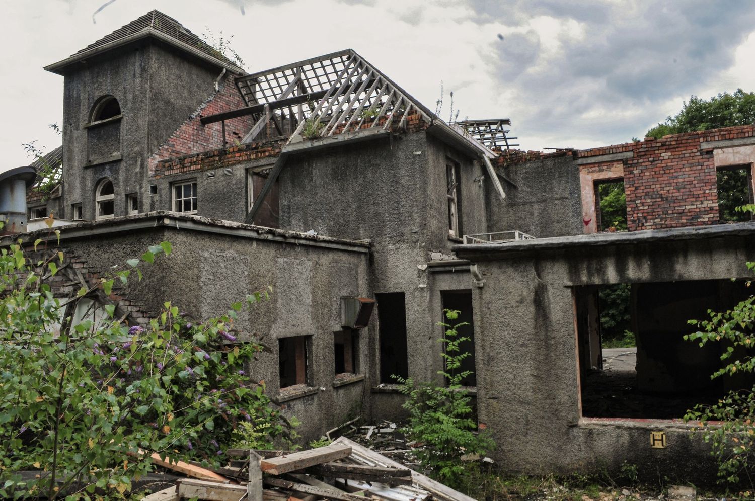 Crumbling multi-storey building overtaken by vegetation, with broken roofs, exposed brickwork, and shattered windows mountain ash hospital