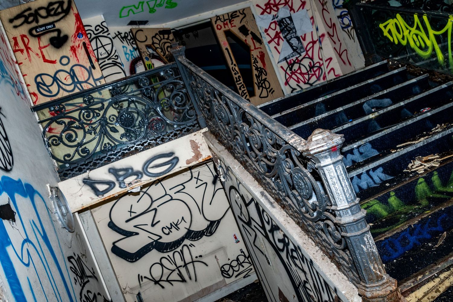Graffiti-covered staircase in an abandoned building, with ornate metal railings and peeling walls. spin bowling cardiff. urbex abandoned