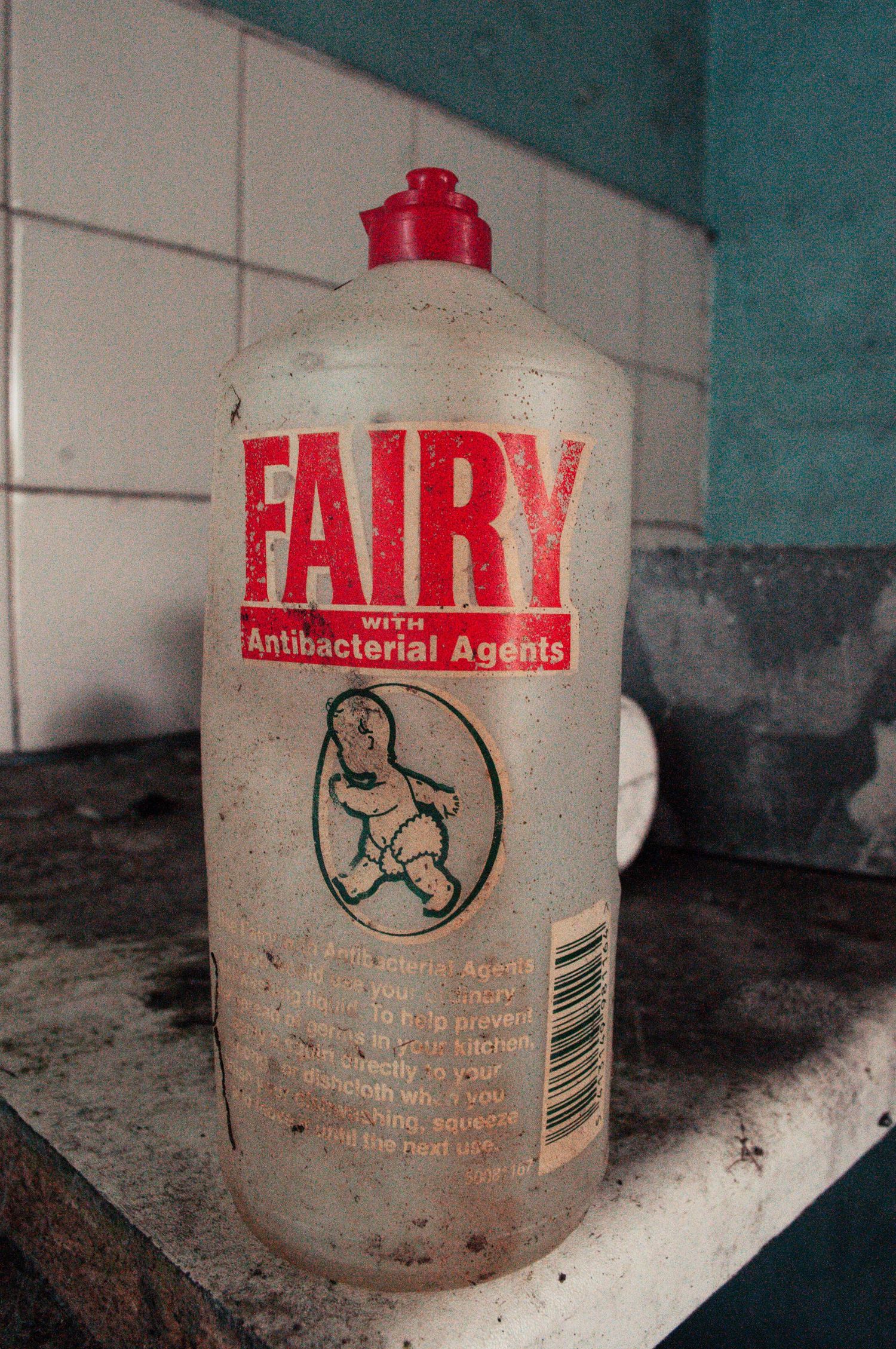 Dirty, half-empty Fairy liquid bottle sitting on a grimy countertop inside an abandoned building. cwm coke works beddau
