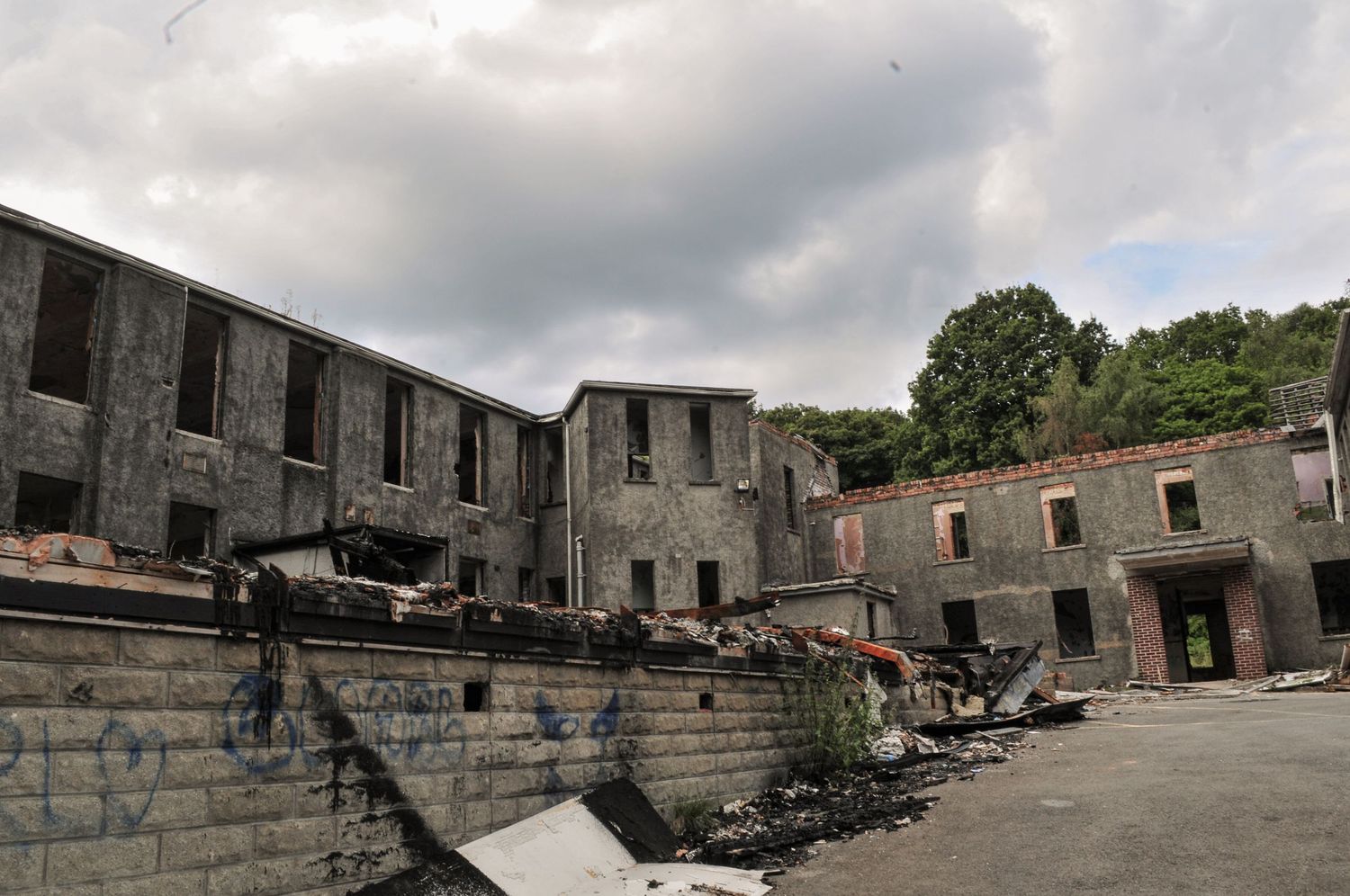 Wide view of a decaying courtyard surrounded by empty stone buildings, with rubble and debris scattered  mountain ash hospital