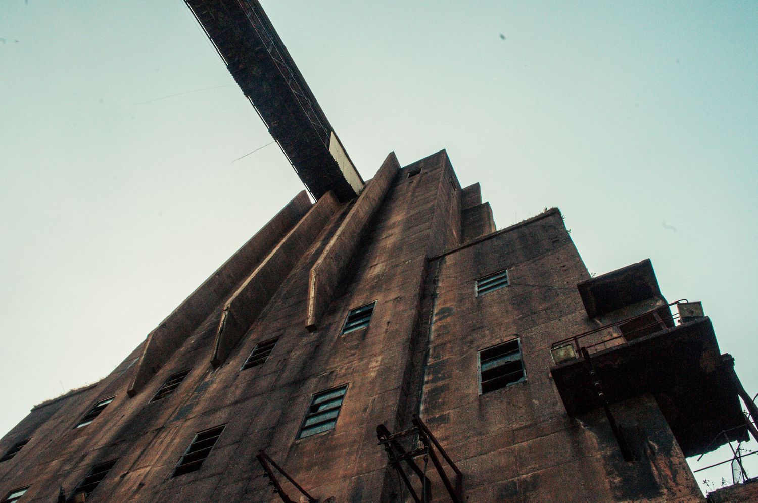 Upward view of a massive concrete industrial building with an elevated conveyor bridge extending above it. cwm coke works beddau. ash olion