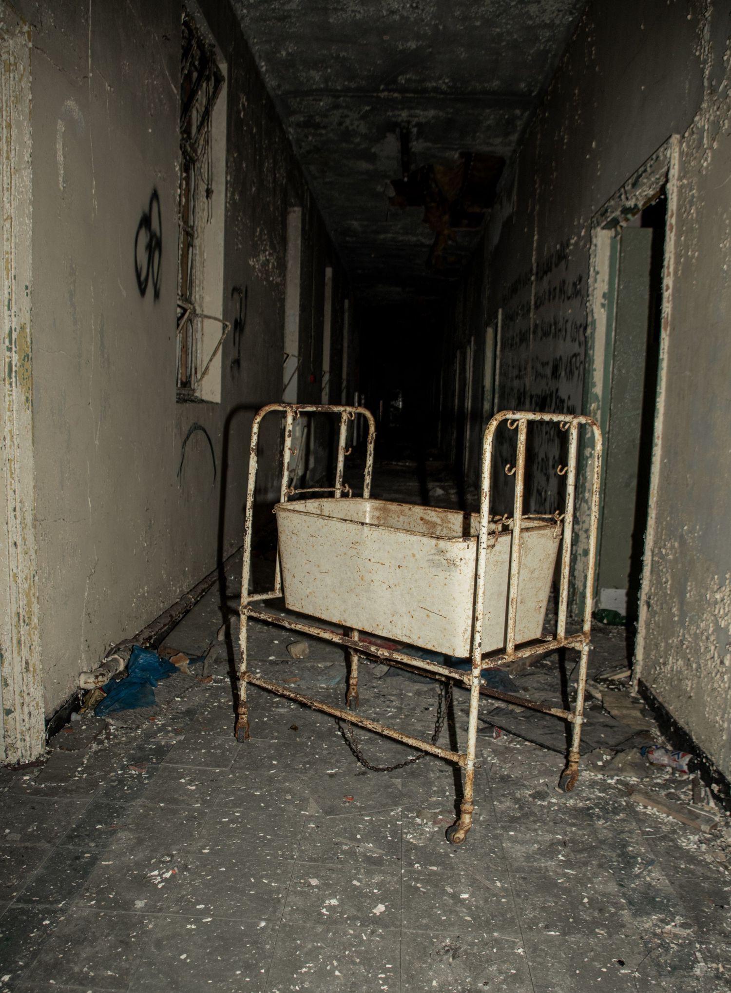 Rusty metal hospital cot left in the middle of a dark, crumbling corridor inside an abandoned building. amman valley maternity hospital