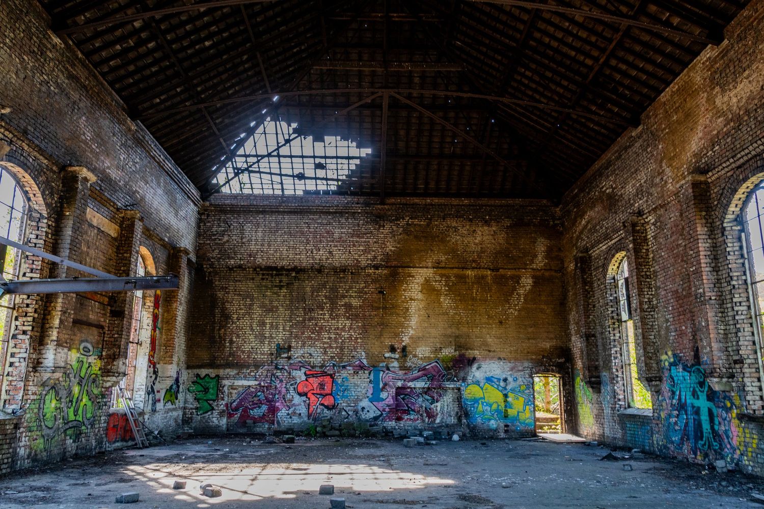 Spacious abandoned brick hall with a broken skylight and colourful graffiti covering the interior walls. ash olion photography. welsh coal