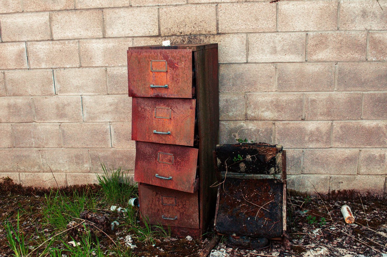 Stack of rusted metal filing cabinets placed against a concrete block wall, surrounded by weeds. cwm coke works beddau wales.