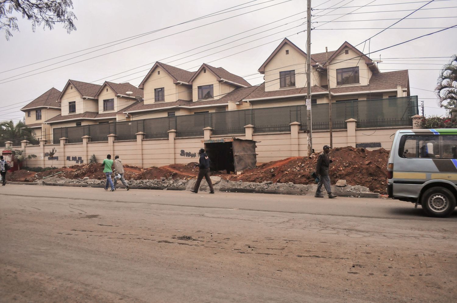 Wide street view of a long row of modern houses with pedestrians walking along the road in front. Kenya, Africa