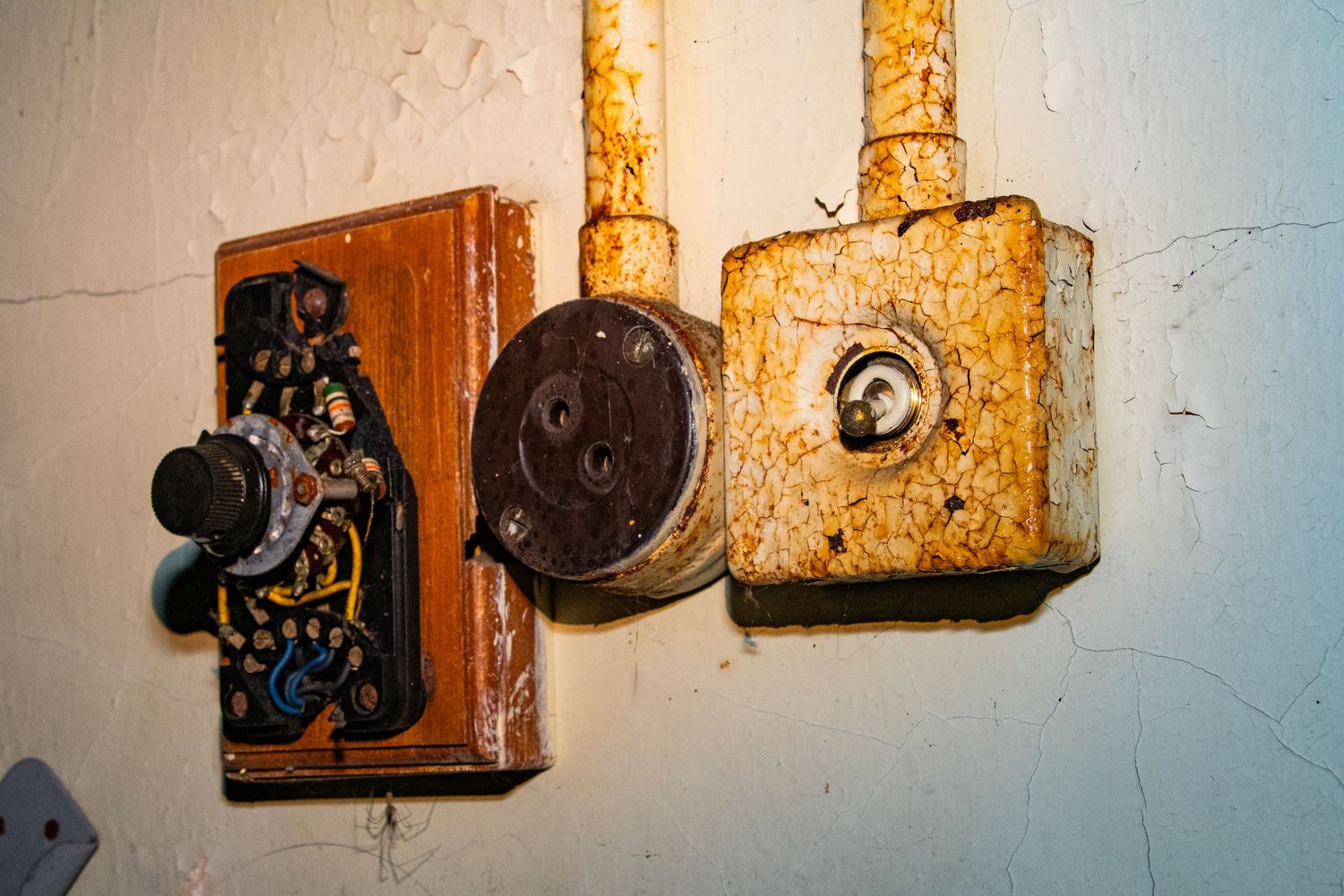 Close-up of old rusted electrical switches mounted on a cracked, peeling wall inside an abandoned building. amman valley maternity hospital