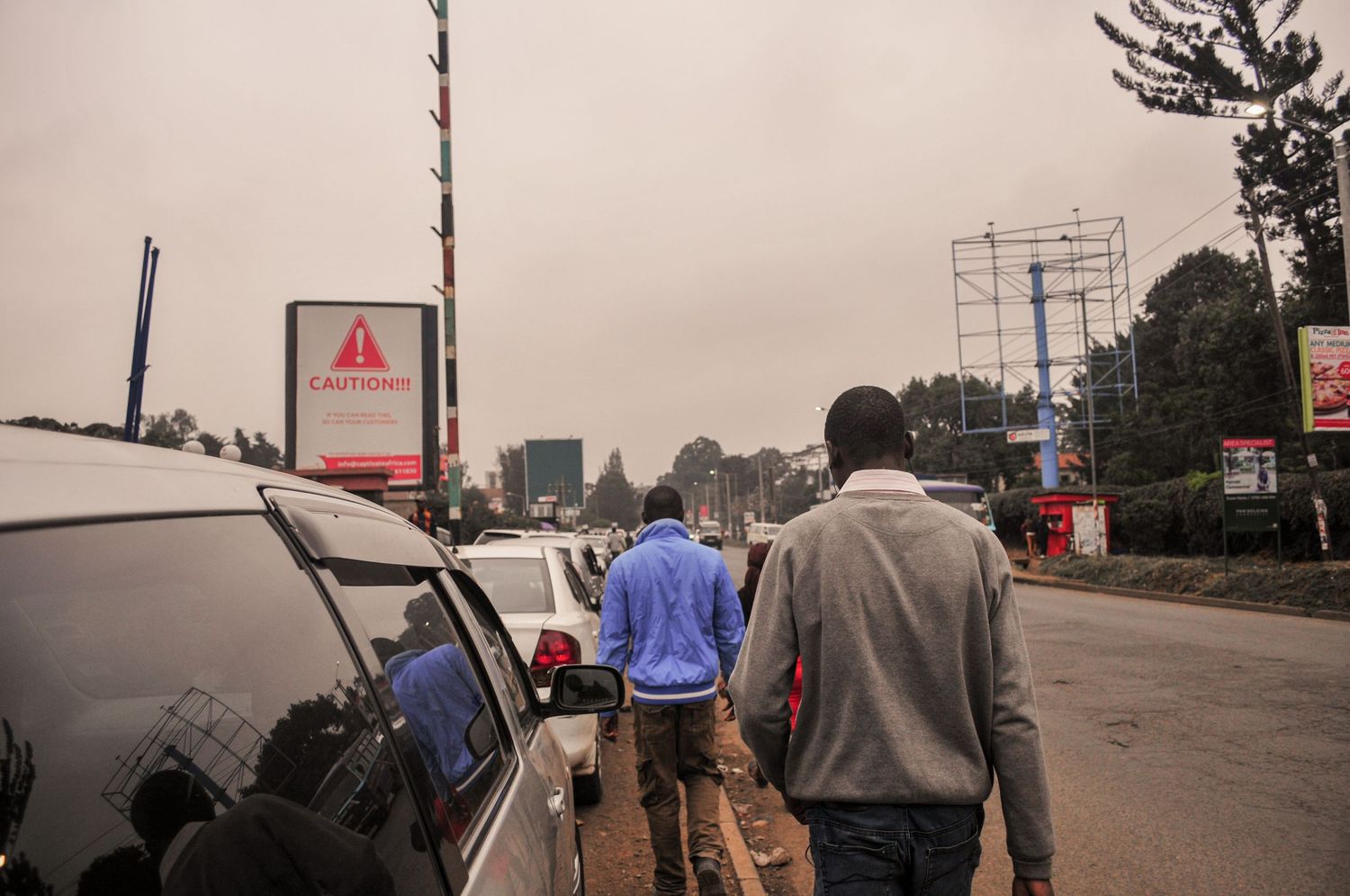 Busy roadside scene with pedestrians walking parked cars under an overcast sky. ash olion Kenya, Africa