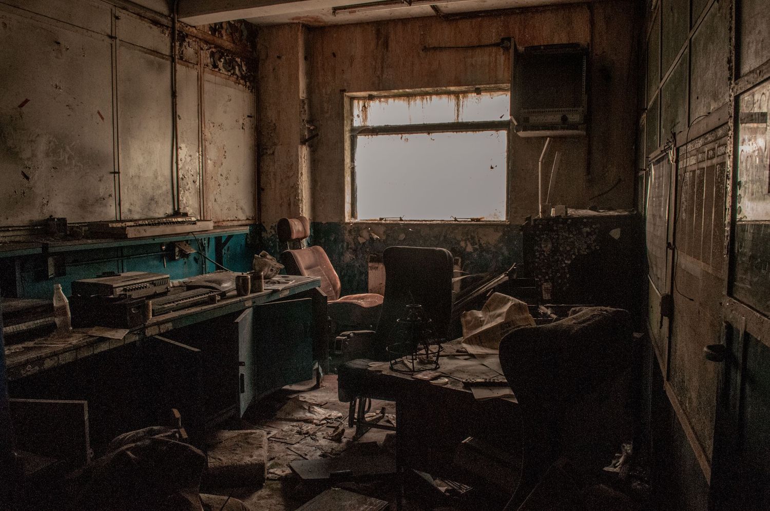 ash olion. Derelict office with broken desks, scattered debris, peeling walls, lit by faint daylight through grimy windows. cwm coke works