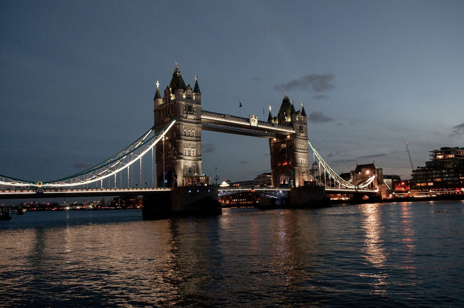Evening view of Tower Bridge lit up over the River Thames, with its lights reflecting across the dark water