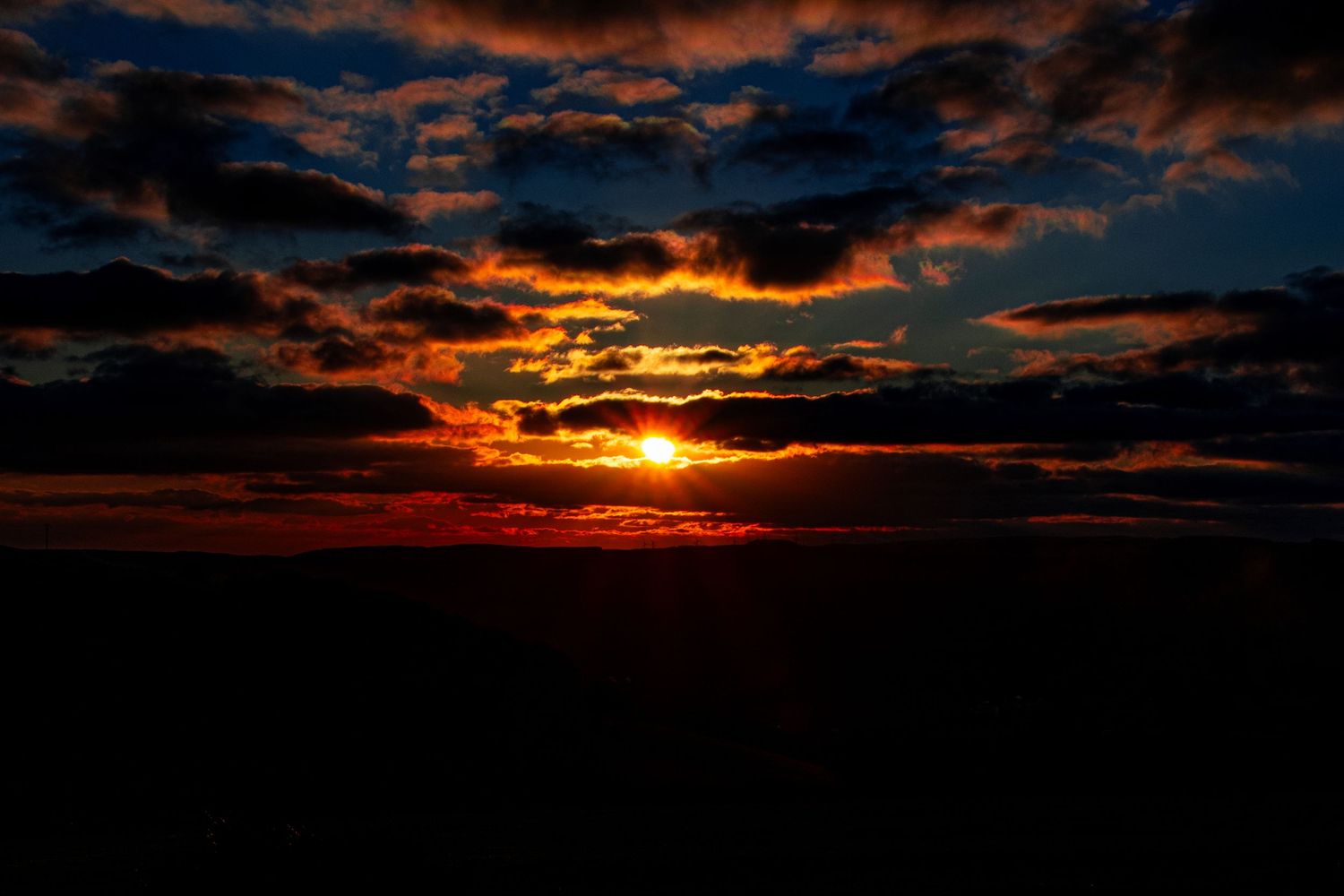 Fiery sunset over the horizon with dramatic dark clouds and a glowing orange sun. ash olion photography. nature, skies, fine art photography
