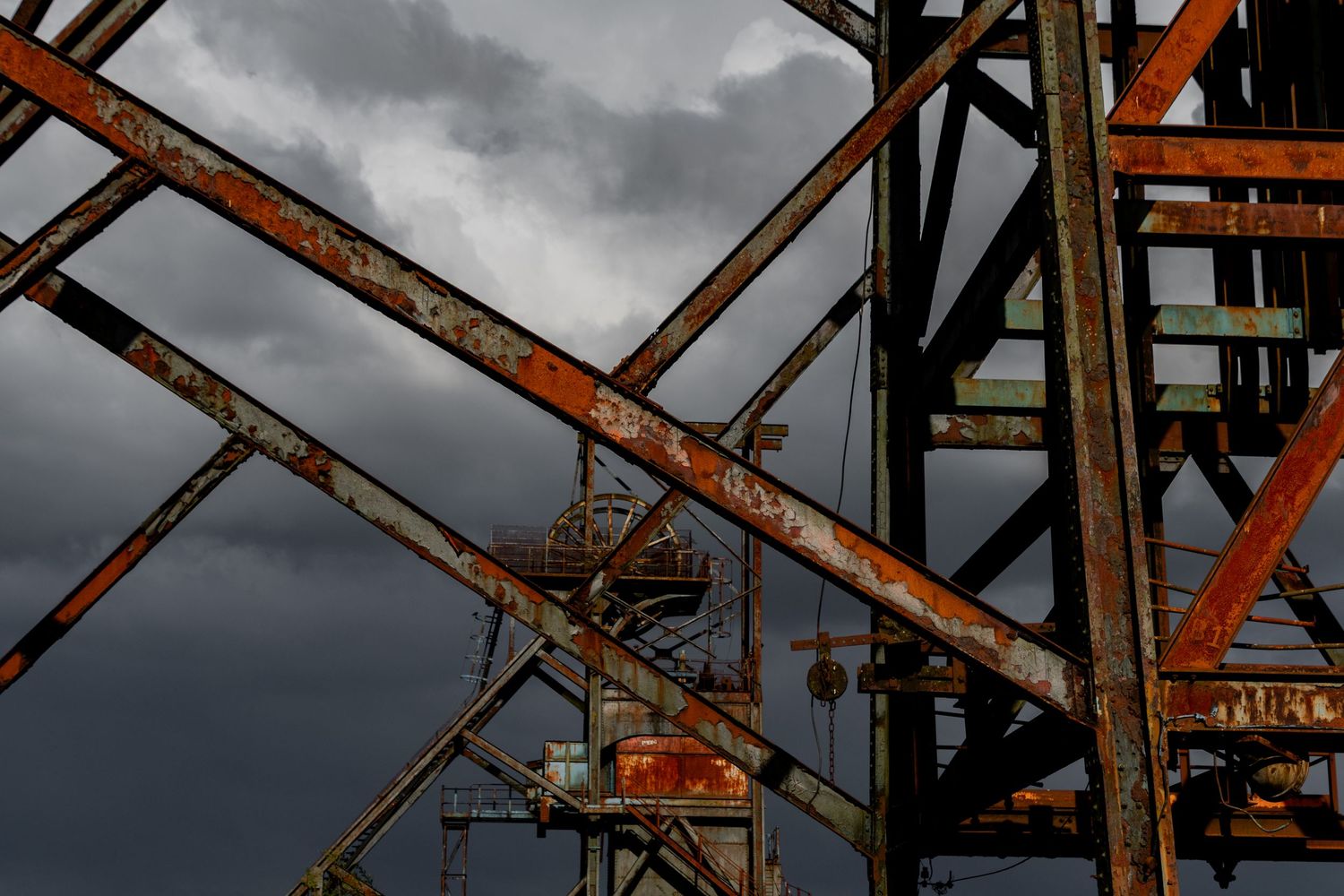Rusted steel headstocks rising into a dark, cloudy sky, with intersecting beams and platforms. mine headstock penallta colliery. ash olion