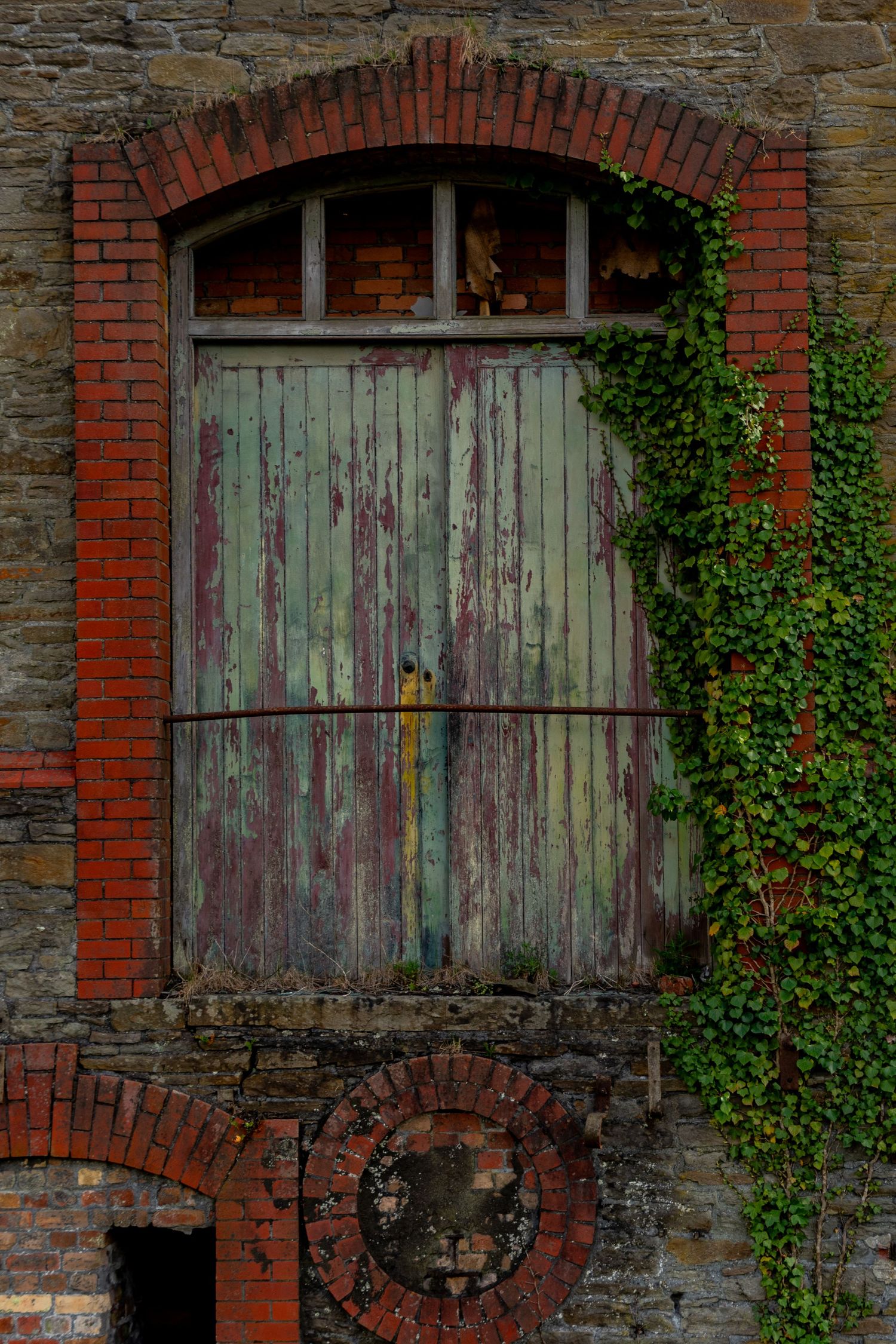 Weathered wooden doors set within a brick archway of an abandoned industrial building,  covered in ivy. penallta colliery wales ash olion