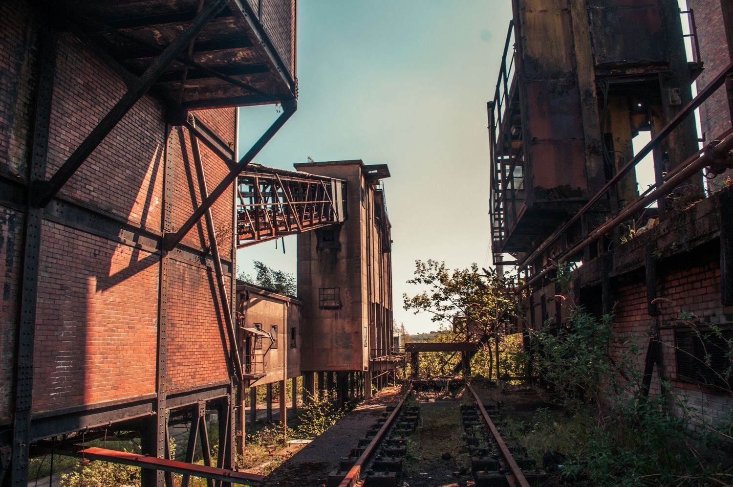 Rusted elevated walkway and metal structures in an abandoned industrial site, lit by warm late-day sunlight. cwm coke works beddau ash olion