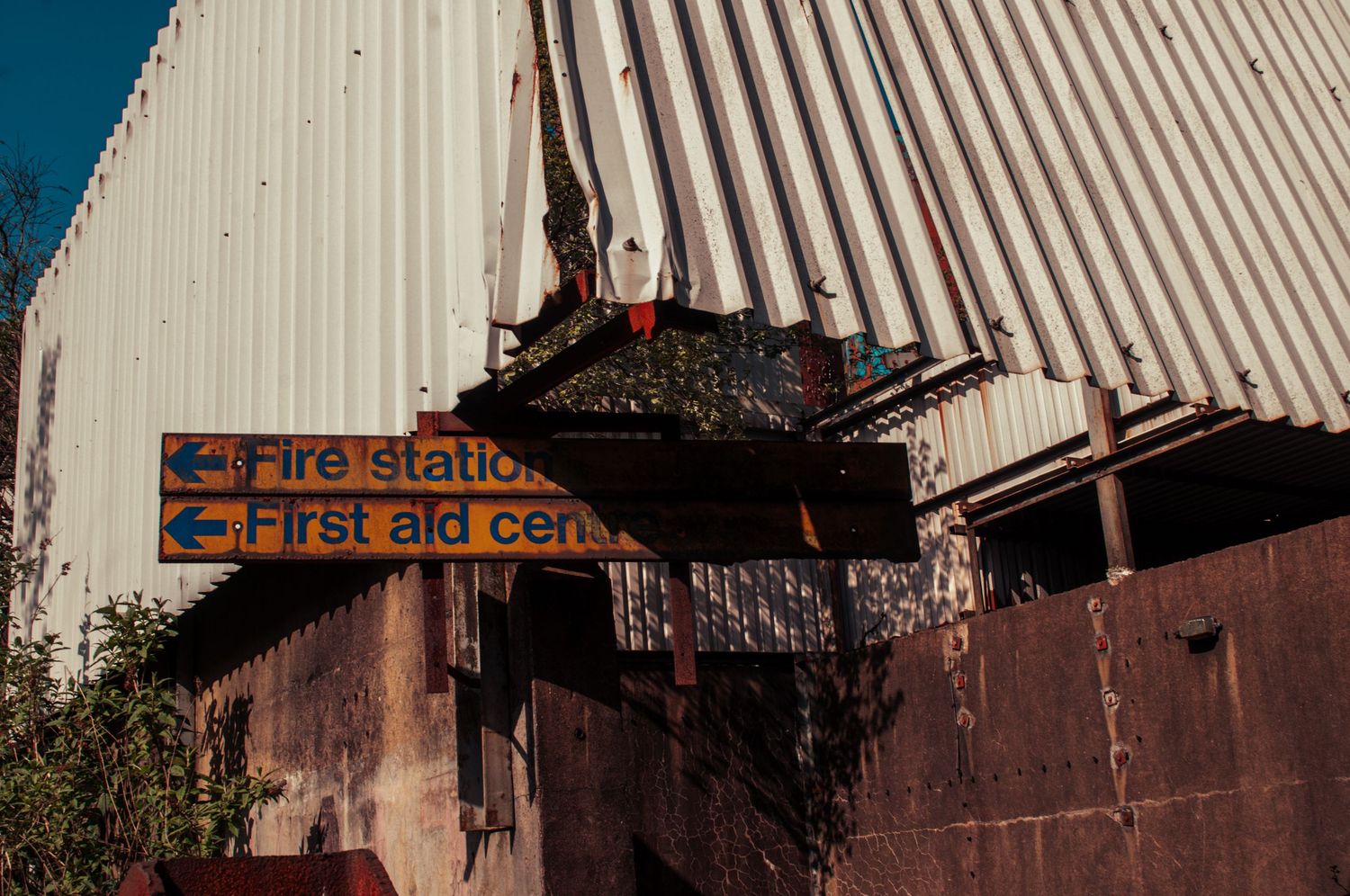 Weathered industrial building with bent corrugated metal roofing and faded signs pointing to a fire station and first aid centre  cwm coke