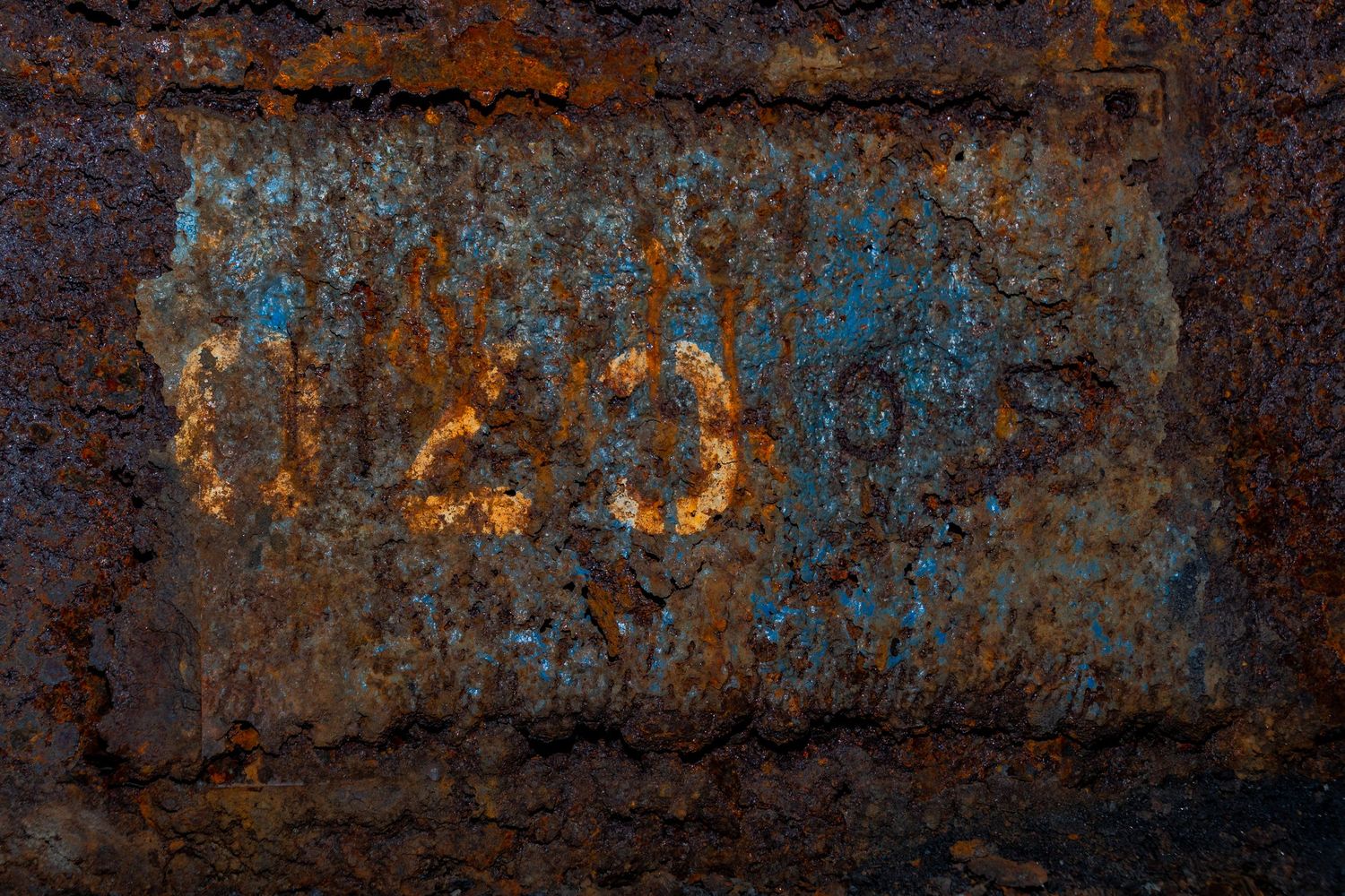 Close-up of heavily rusted metal surface with peeling blue paint and faint yellow numbers. penallta colliery ash olion photography. wales
