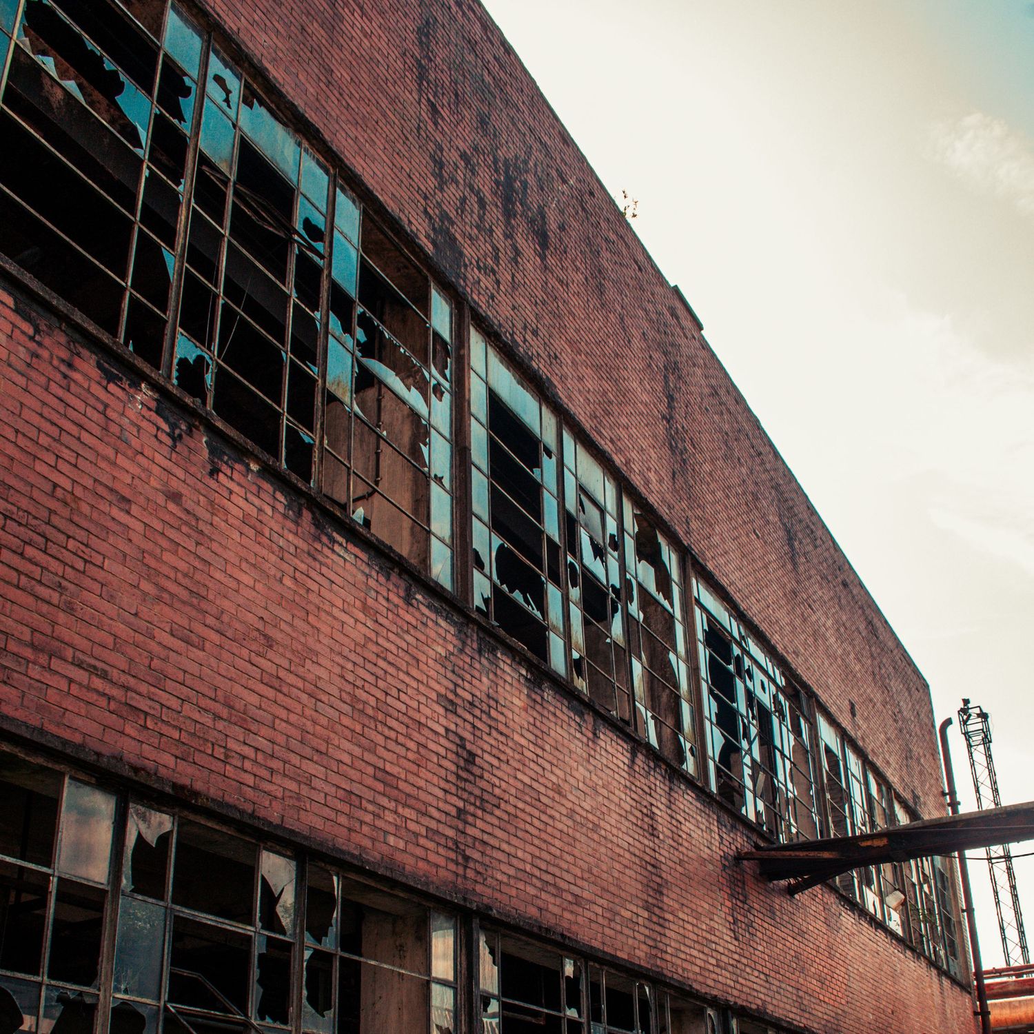 Long brick industrial building with rows of shattered windows and a rusted metal beam jutting outward