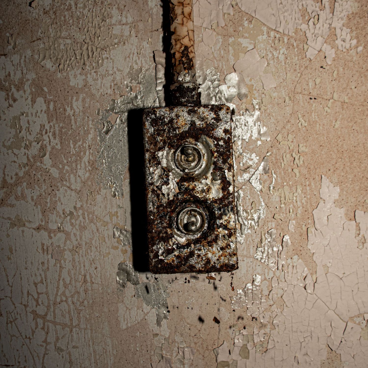 Close-up of a heavily rusted electrical switch box mounted on a peeling, stained wall inside an abandoned building. amman maternity hospital